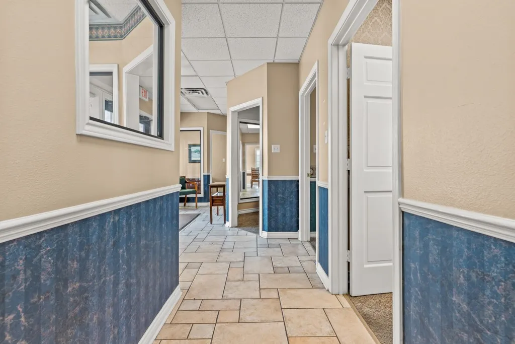 Corridor featuring neutral-toned walls, blue wainscoting, white trim, and a drop ceiling