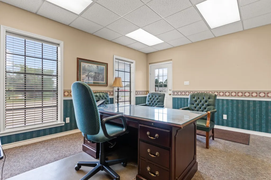 Office space featuring carpet flooring, drop ceiling with integrated lighting, and walls with a decorative border and wainscoting