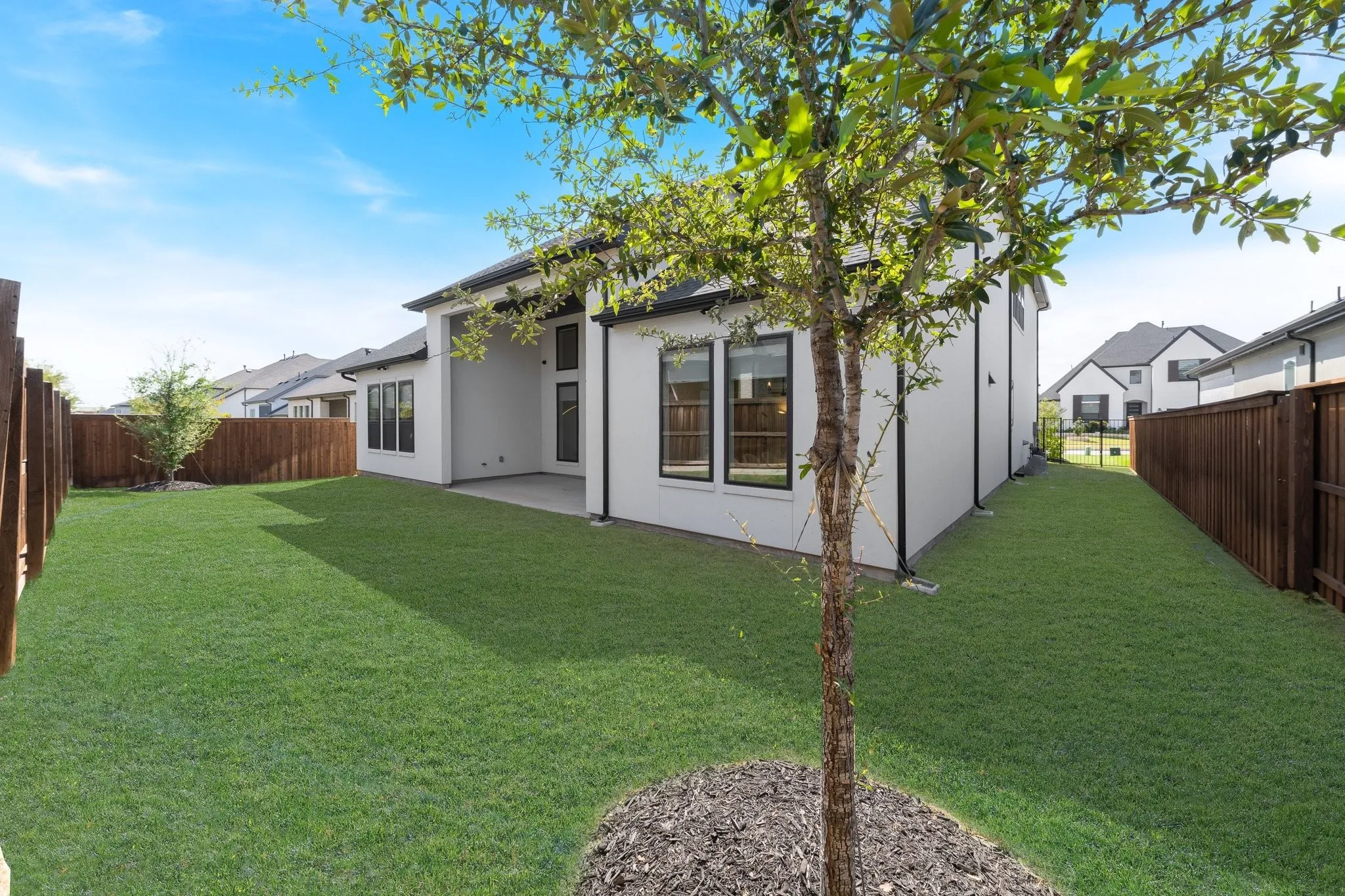 Expansive backyard featuring a manicured lawn, established privacy fencing, a covered patio, and modern black-framed windows