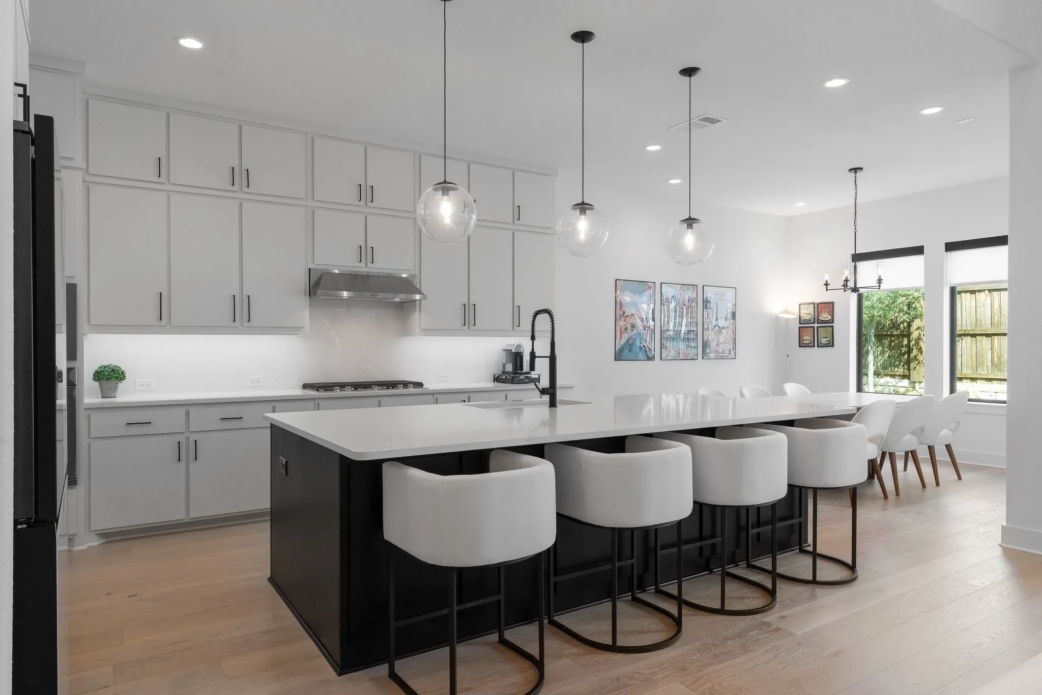 Modern kitchen featuring light-toned cabinetry, a black kitchen island with a white countertop, stainless steel range hood, and light wood-finish flooring