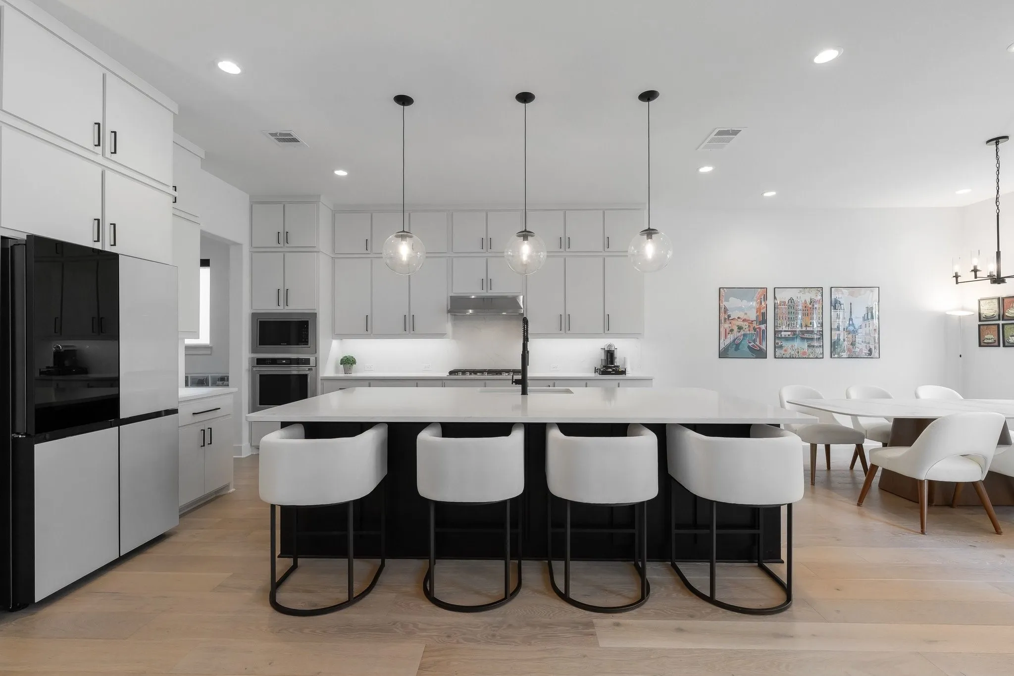 Gourmet kitchen with an expansive island, light wood-finish flooring, white cabinetry, integrated double ovens, and recessed lighting