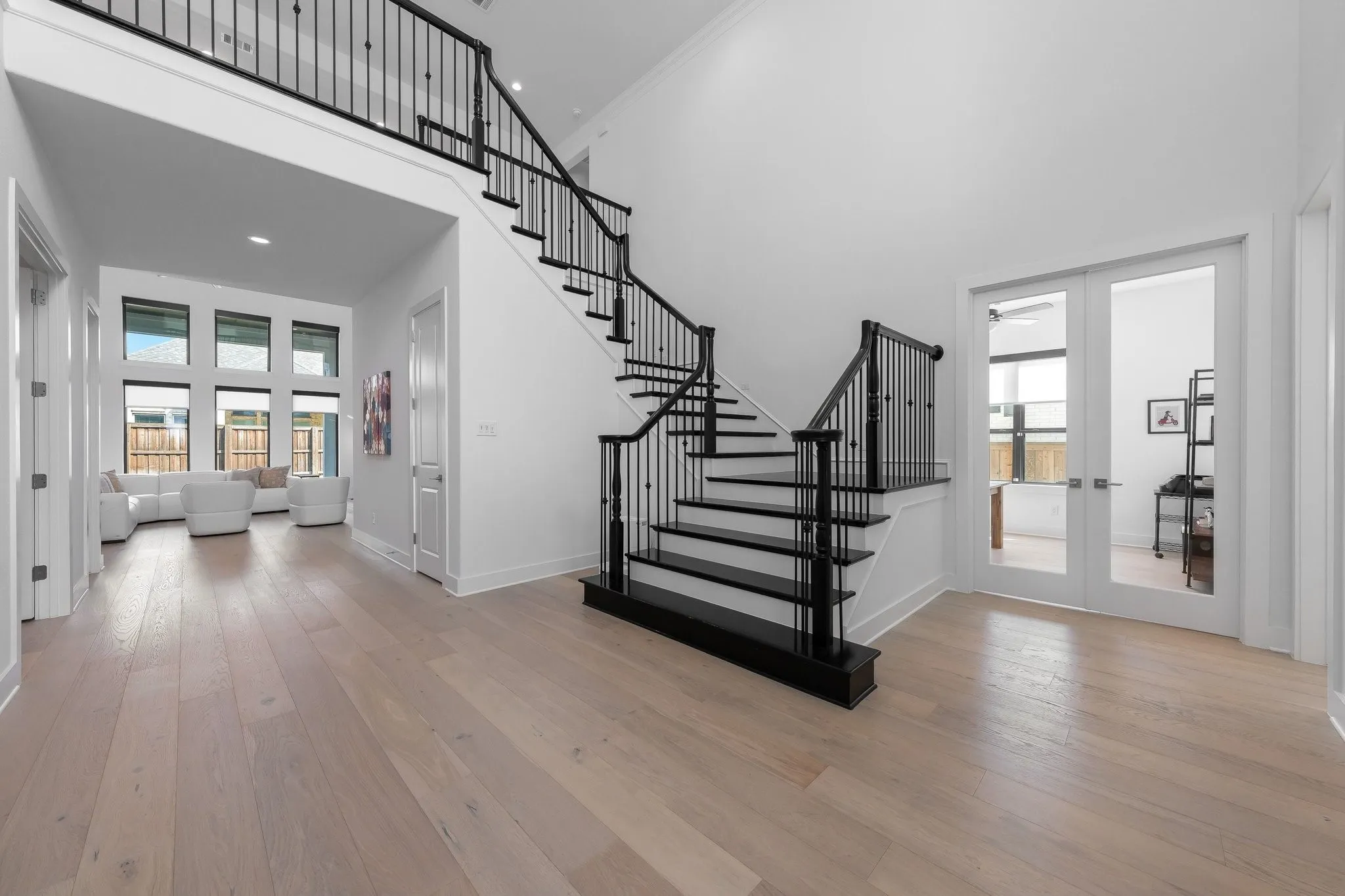 Sweeping staircase with black wrought iron balusters, light wood-finish flooring, and a two-story ceiling