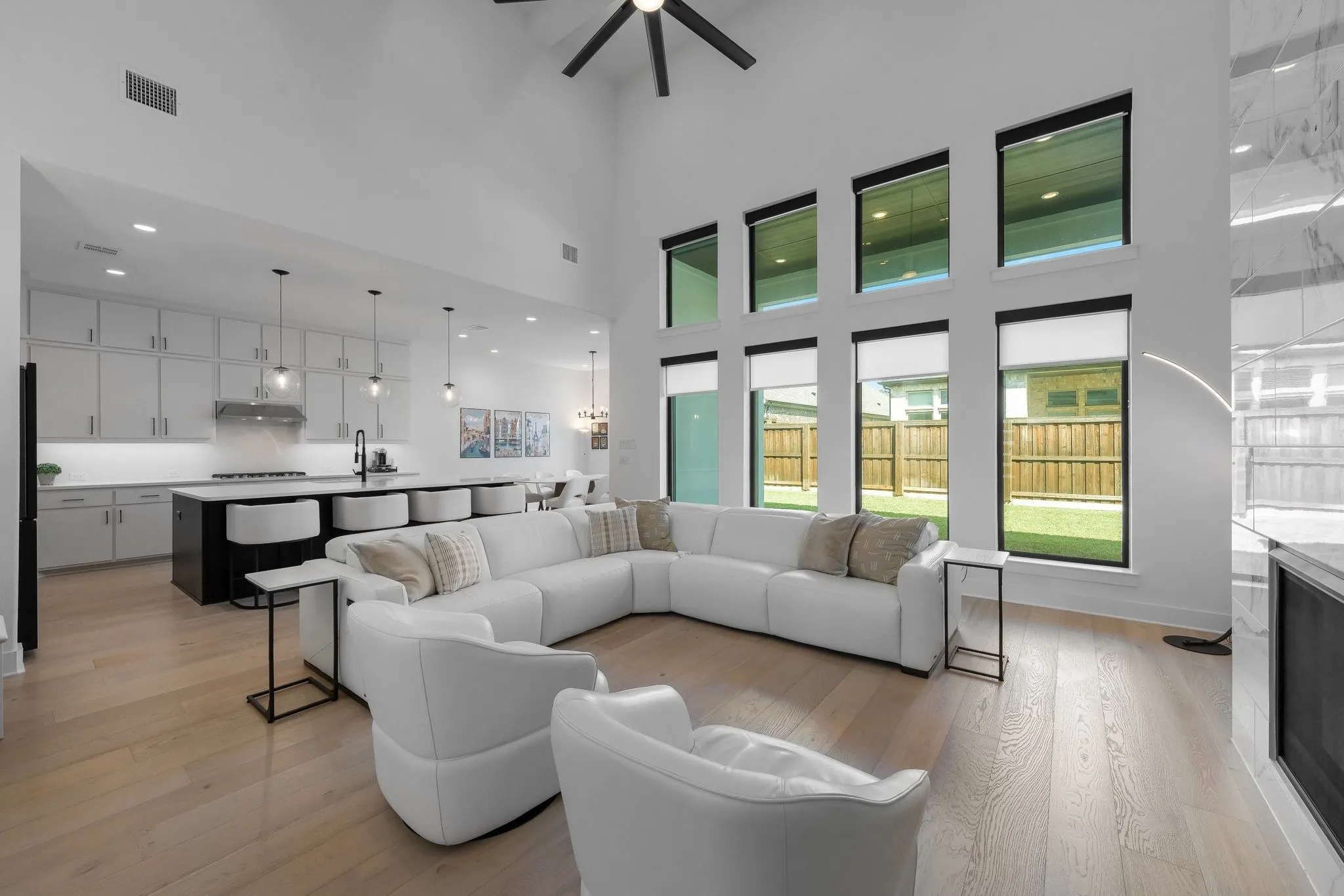 Vaulted ceiling with a ceiling fan, light wood-finish flooring, full-height windows, a modern fireplace, and a kitchen featuring an island with built-in seating
