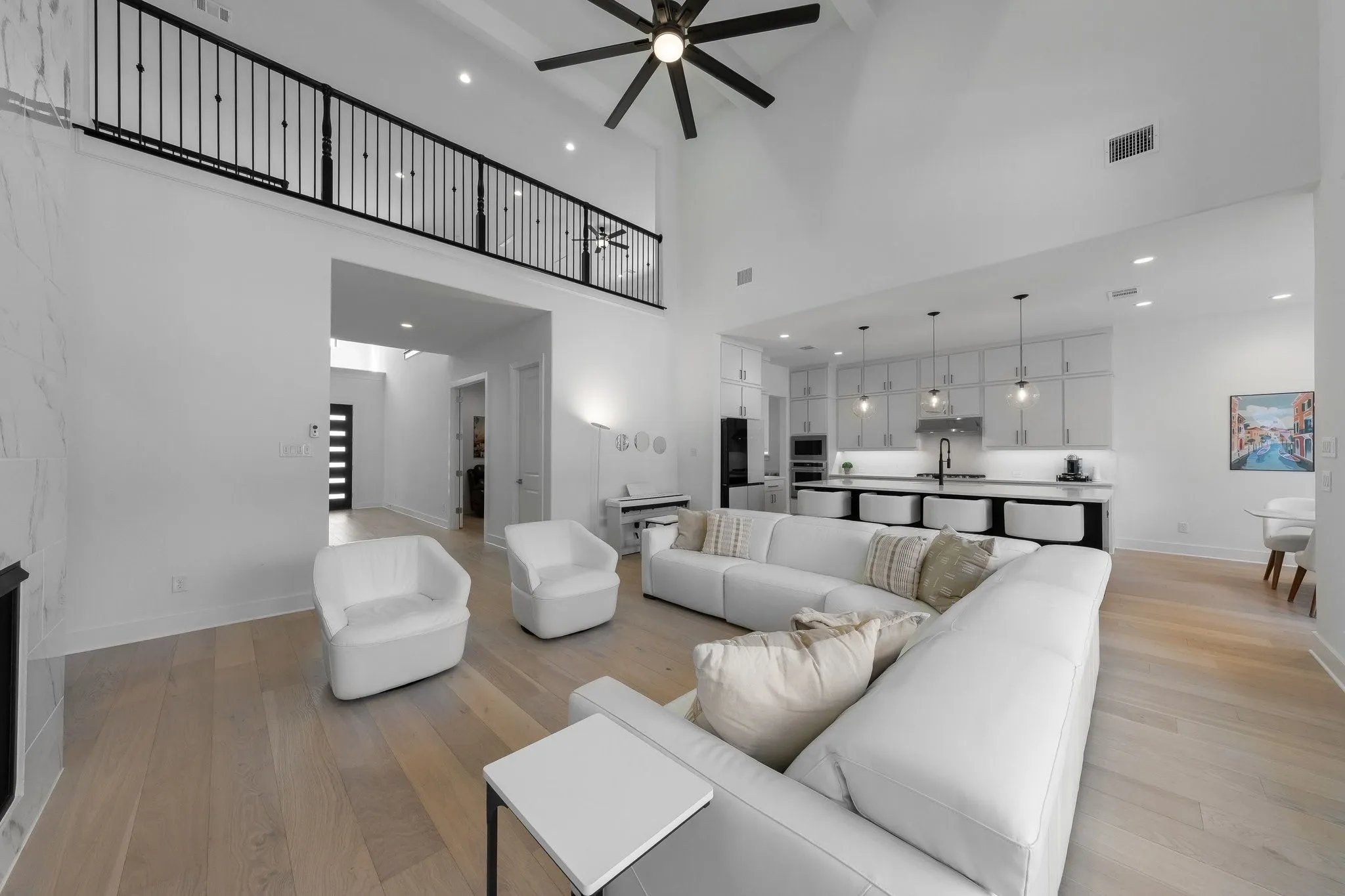 Vaulted ceiling with a ceiling fan, light wood-finish flooring, and an open loft with a black metal railing