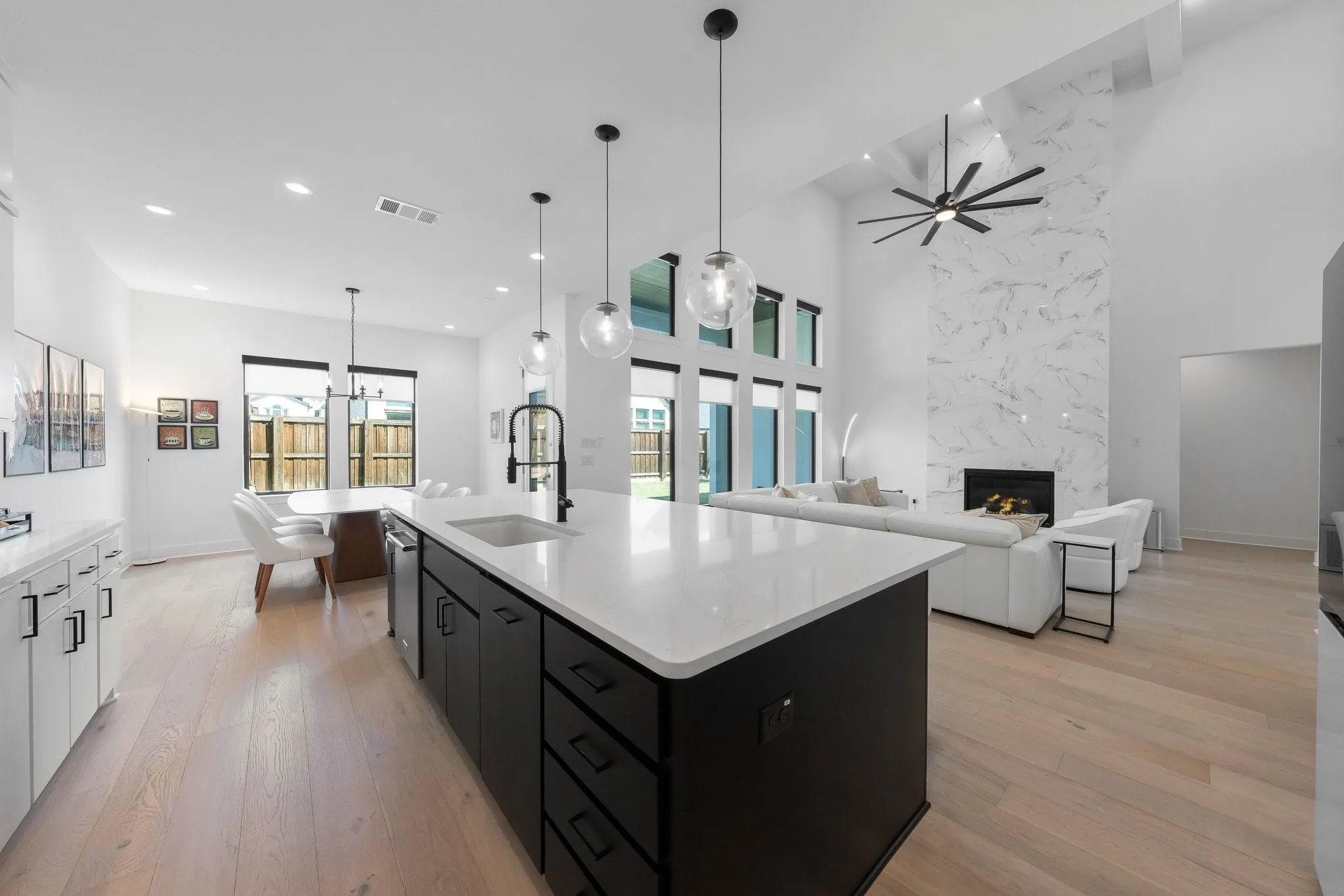 Spacious kitchen island with a white countertop and dark cabinetry, wood-finish flooring, a tall fireplace with a marble-patterned surround, and high ceilings with a modern ceiling fan