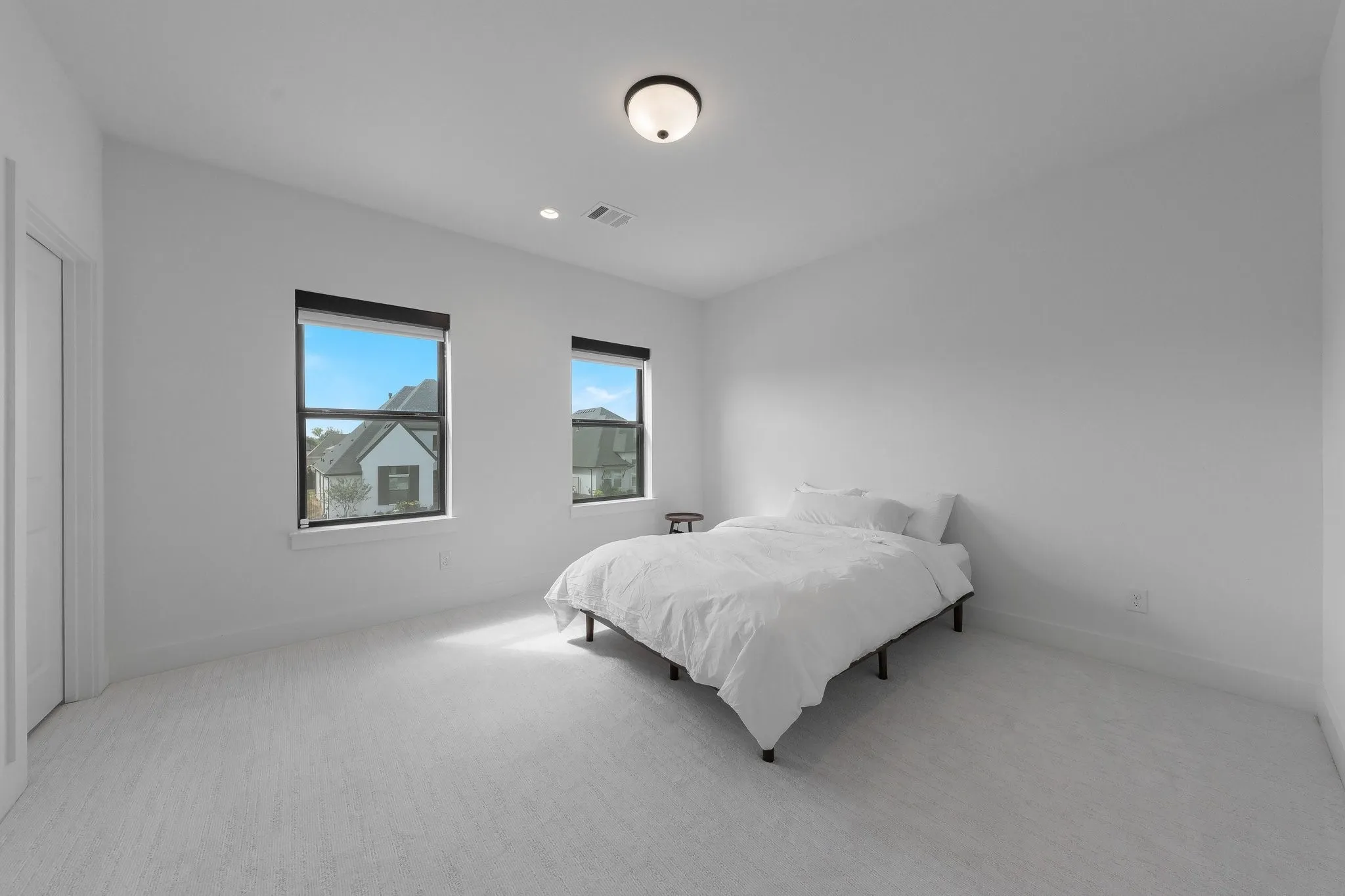 White walls, light-toned carpeting, two windows with black trim, and a ceiling-mounted light fixture