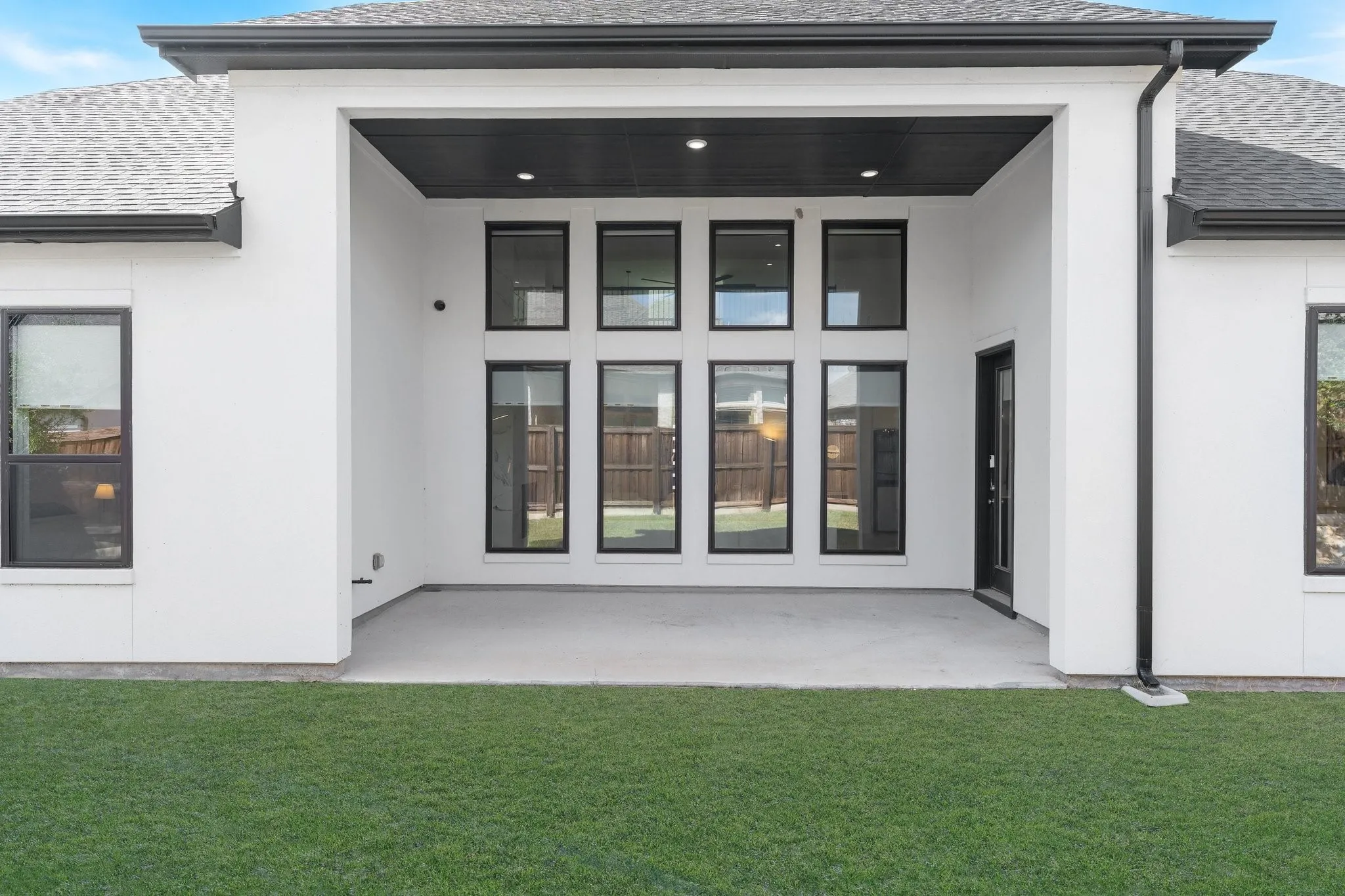 Covered patio with concrete flooring, multiple tall windows, and a black exterior door