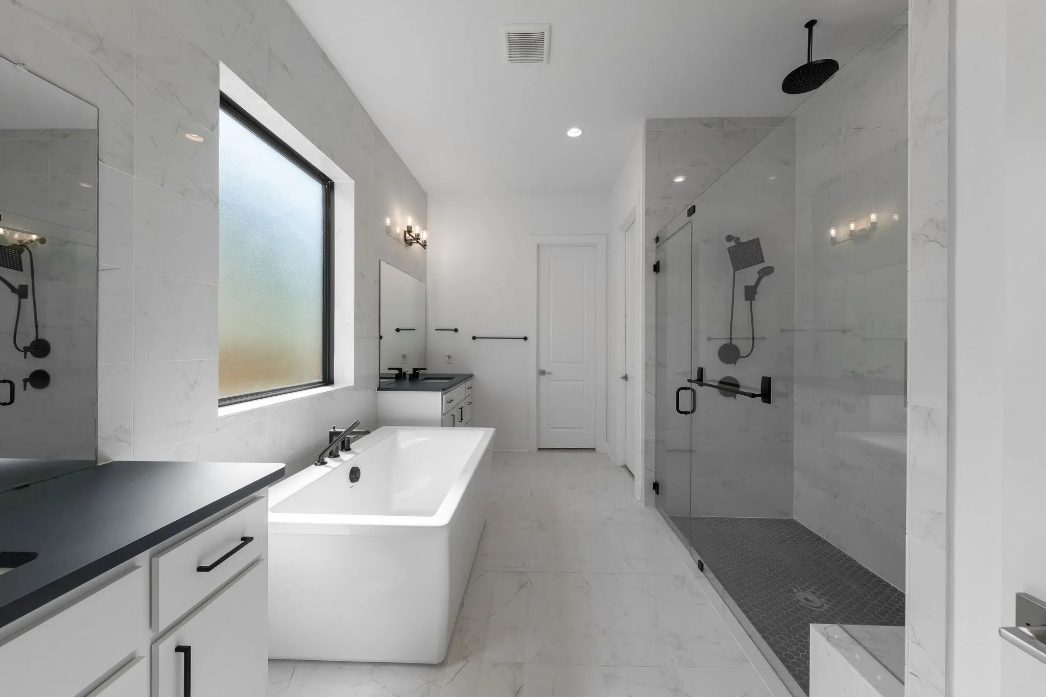 Spacious bathroom featuring a freestanding soaking tub, a large walk-in shower with glass enclosure, dual vanity sinks, white cabinetry, and matte black fixtures throughout