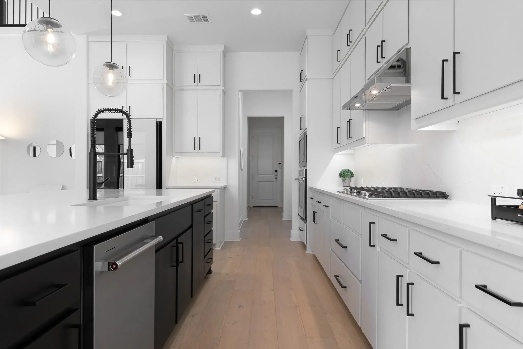 Open-concept kitchen featuring an expansive island, light-toned wood-finish flooring, white cabinetry with black hardware, and an integrated gas cooktop