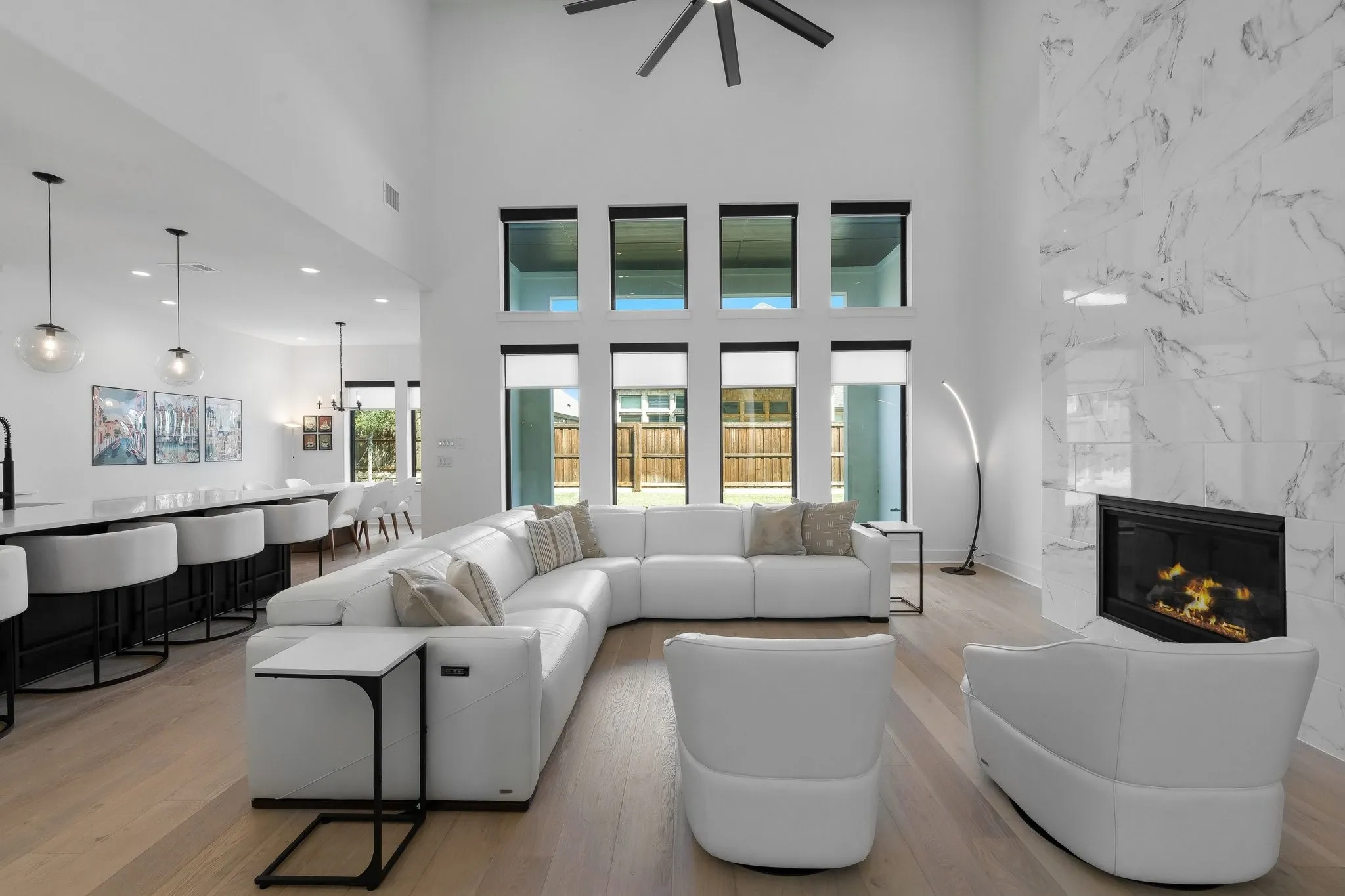 Vaulted ceiling with a ceiling fan, floor-to-ceiling windows, full-height fireplace with stone-finish surround, wood-finish flooring, and built-in kitchen island seating