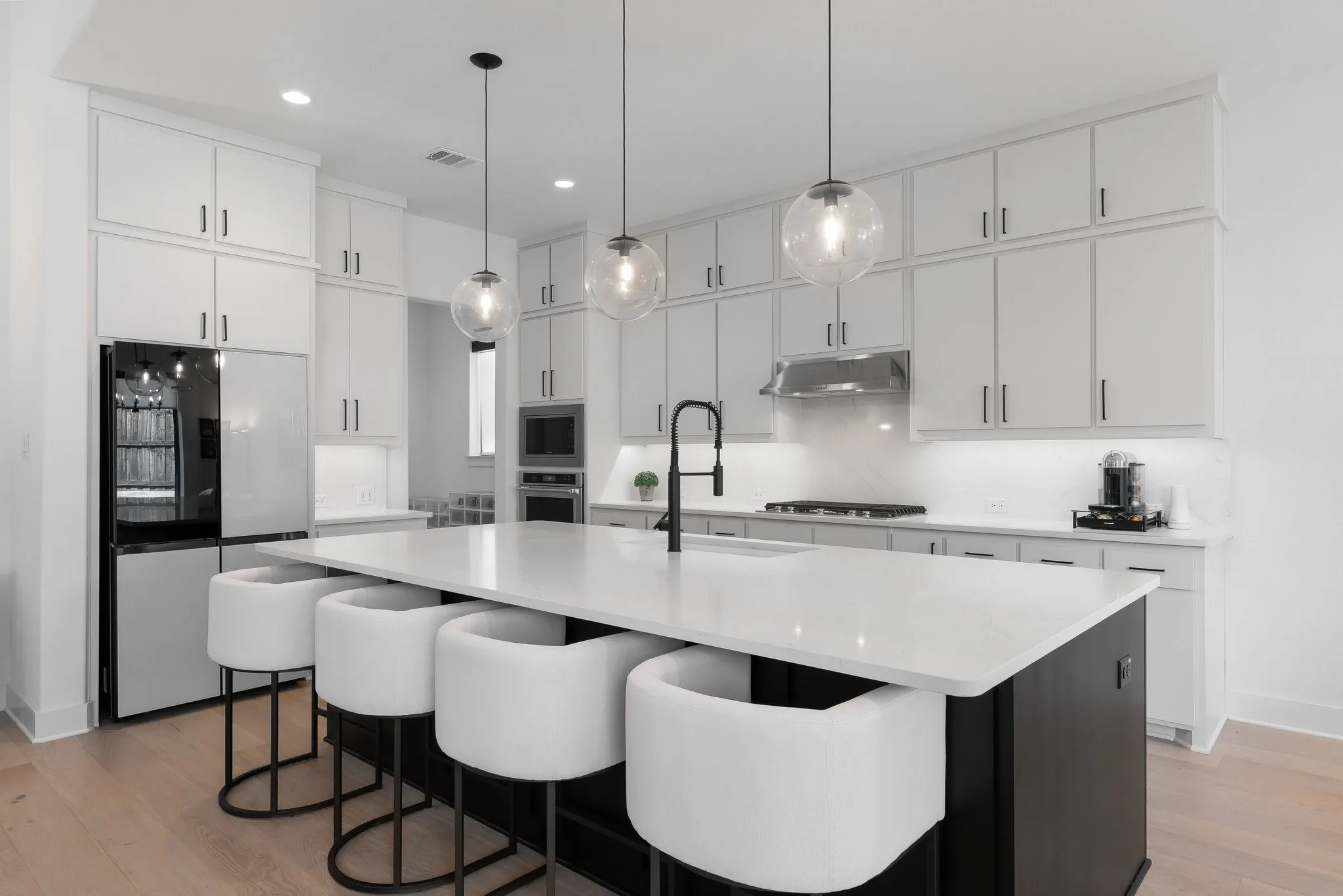 Kitchen featuring an expansive island with a white countertop, white cabinetry with black hardware, wood-finish flooring, a stainless steel range hood, and pendant lighting