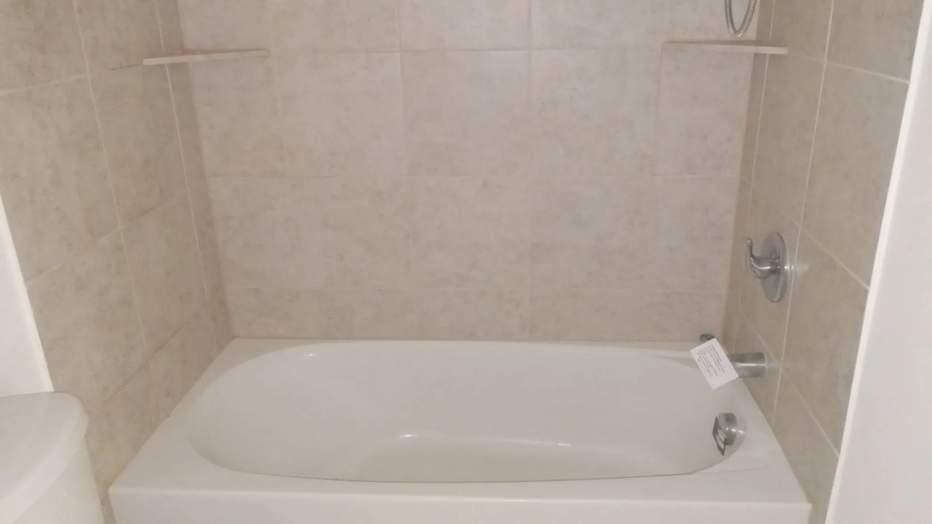Bathtub with tile surround and integrated shelving, featuring a chrome faucet