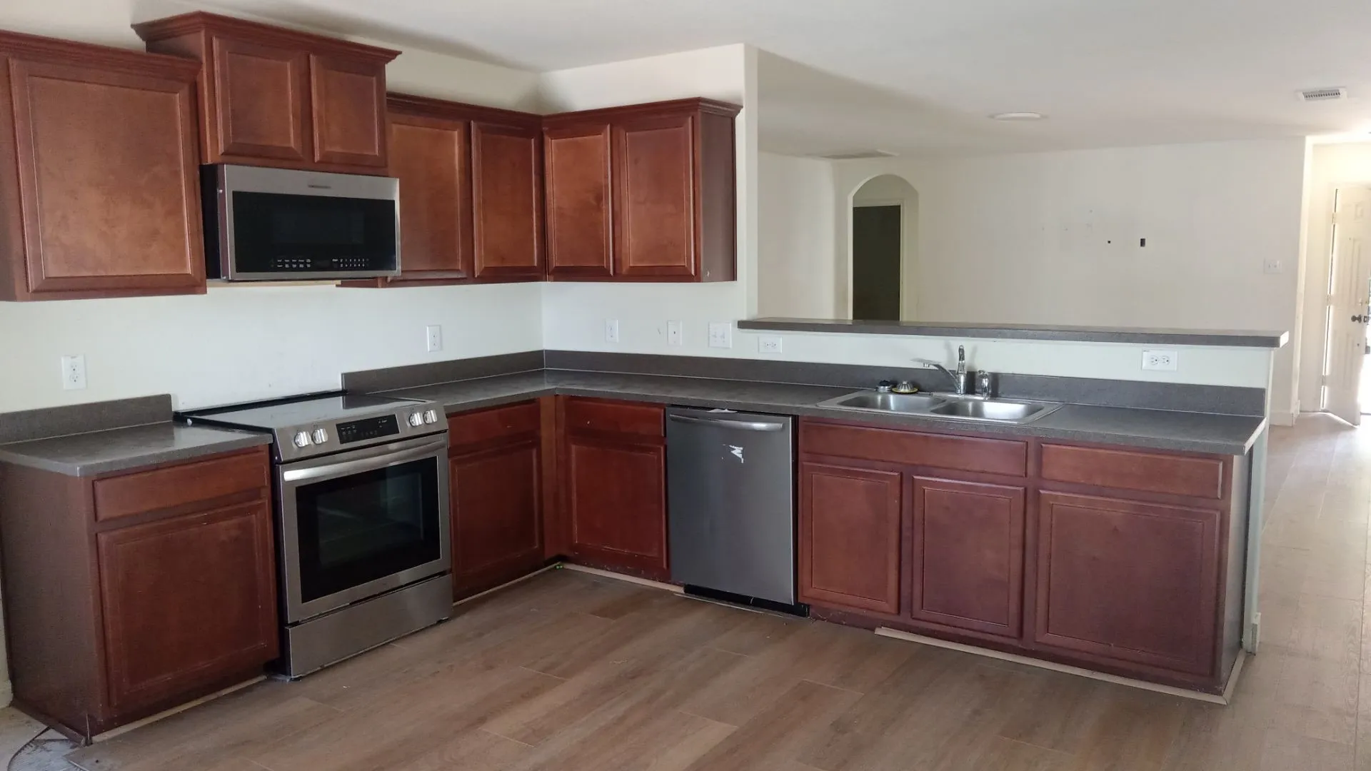 Contemporary kitchen featuring wood-finish flooring, dark wood cabinetry, gray countertops, a stainless steel range, and a stainless steel built-in microwave