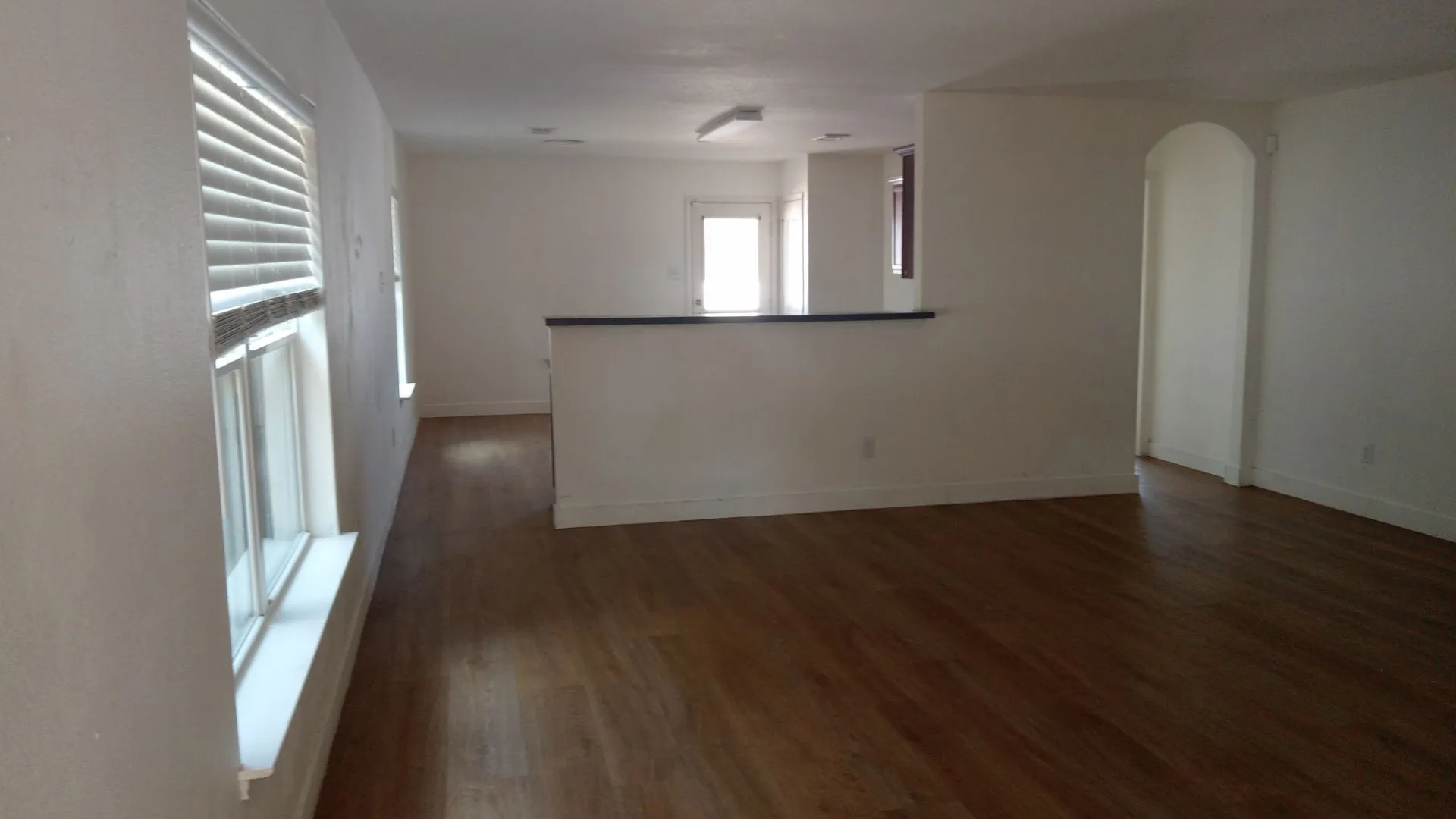 Wood-finish flooring, white walls, multiple windows with blinds, and an arched doorway