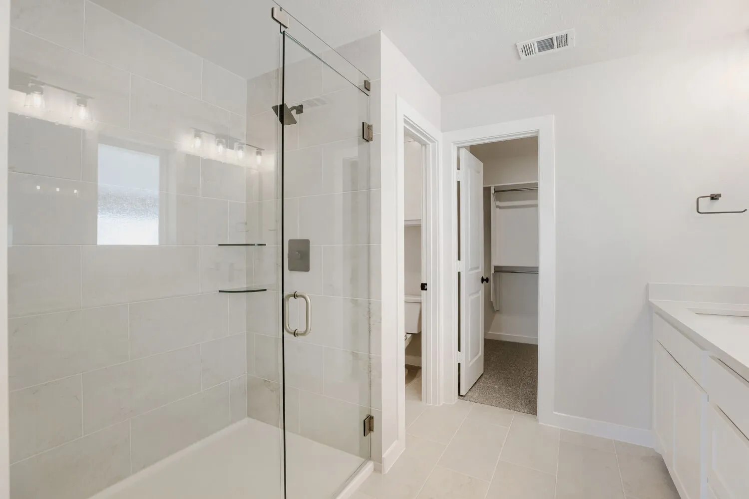 Glass-enclosed shower with tile surround and integrated shelves, dual vanity with undermount sink and quartz countertop, and tile flooring