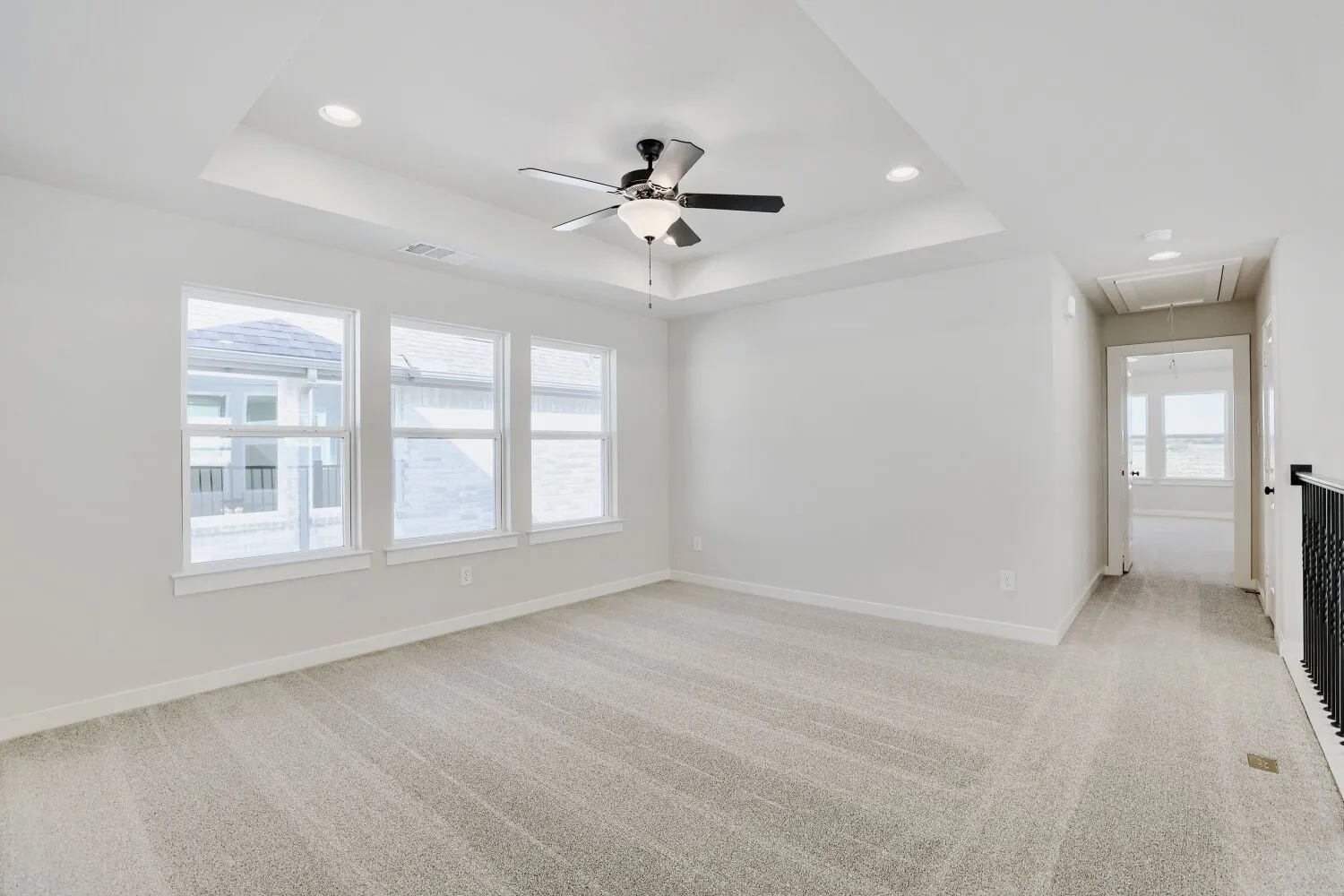 Recessed lighting, tray ceiling, ceiling fan, three windows, and light-toned carpeting