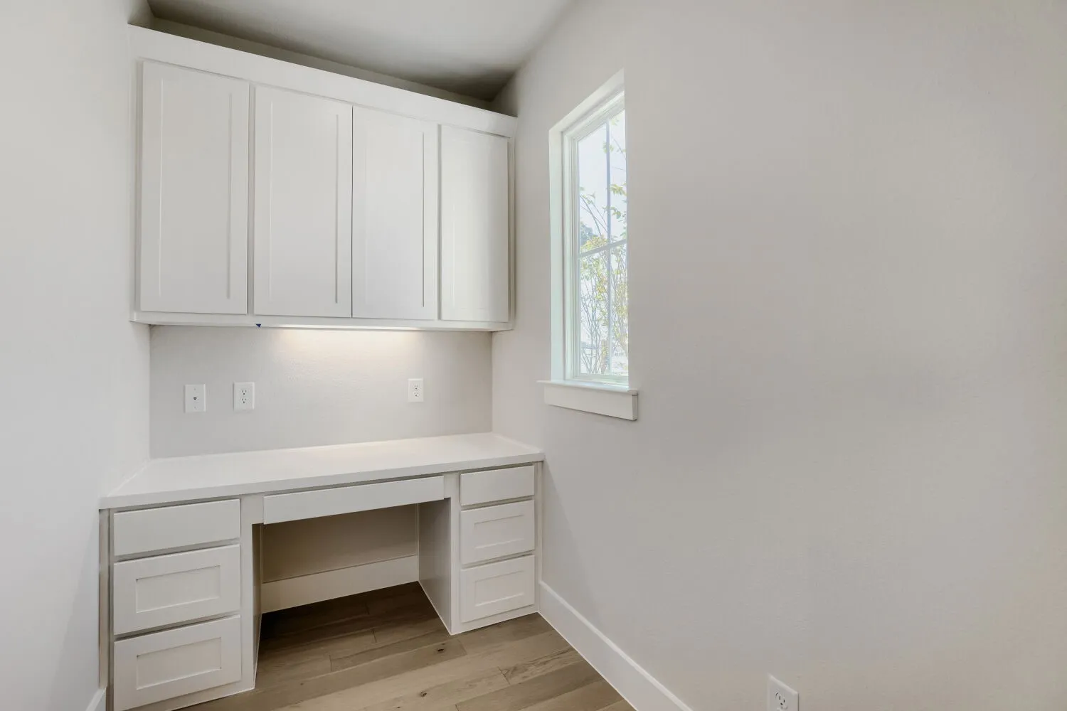 Built-in desk with white cabinetry, under-cabinet lighting, and light wood-finish flooring
