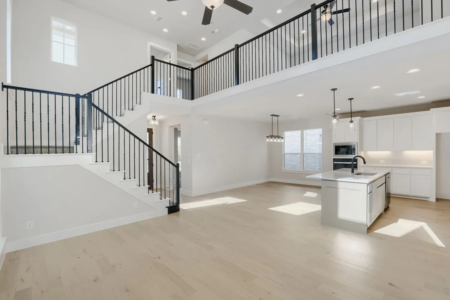 Soaring ceilings, light wood-finish flooring, and an open-concept kitchen featuring an island with a sink and pendant lighting