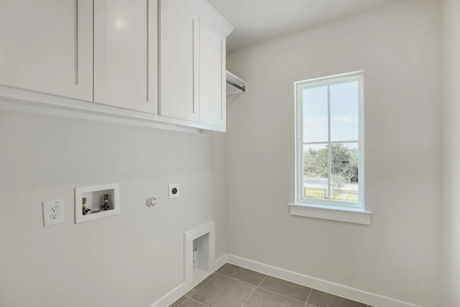 White upper cabinetry, durable tile flooring, single window, integrated utility hookups, and a hanging rod