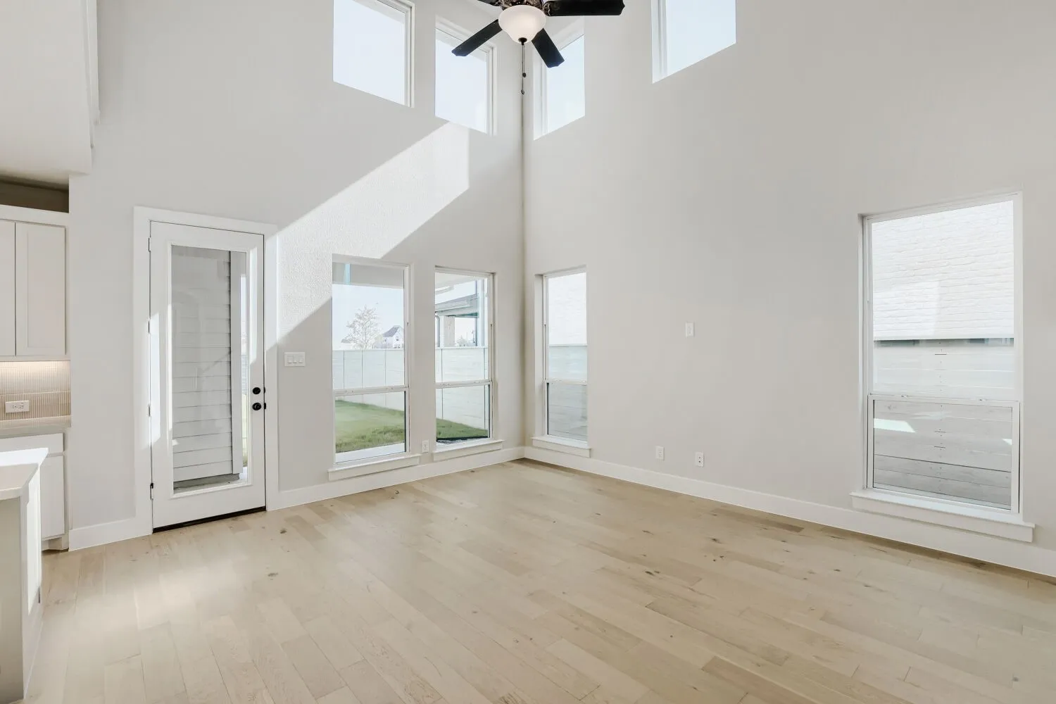Vaulted ceiling, recessed lighting, wood-finish flooring, white cabinetry, and multiple windows