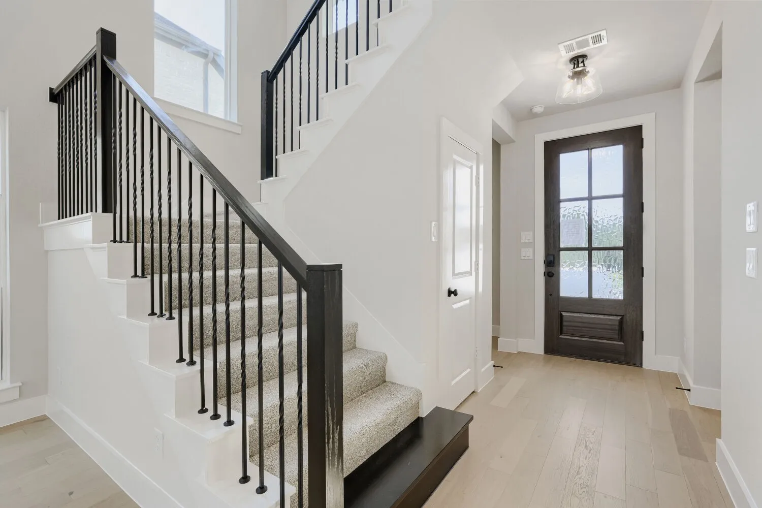 Hardwood-finish flooring, staircase with carpeted treads, black metal balusters, dark wood-finish newel posts, and glass-paneled entry door