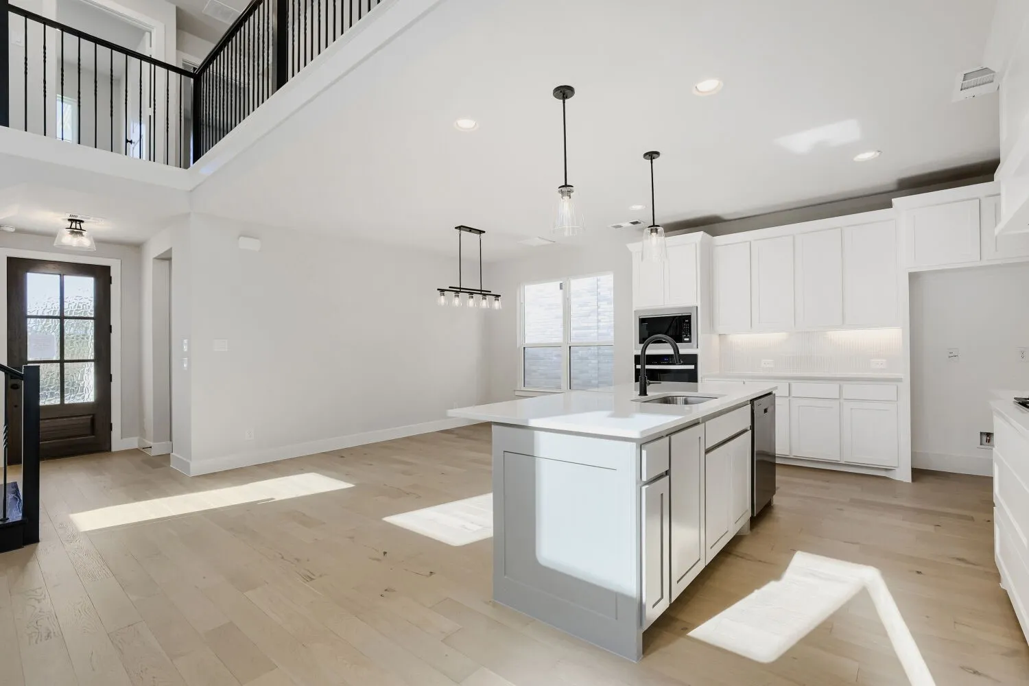 High ceilings, wood-finish flooring, a kitchen island with sink, white cabinetry, and stainless steel appliances