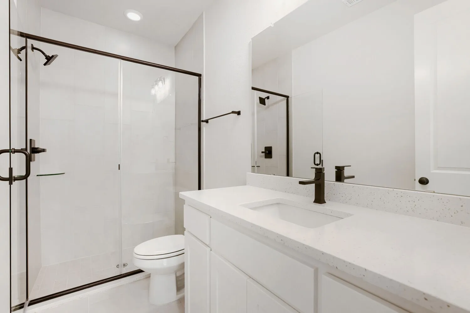 Frameless glass shower enclosure with matte black hardware, white rectangular ceramic tile, and a single vanity with a white solid surface countertop and integrated sink