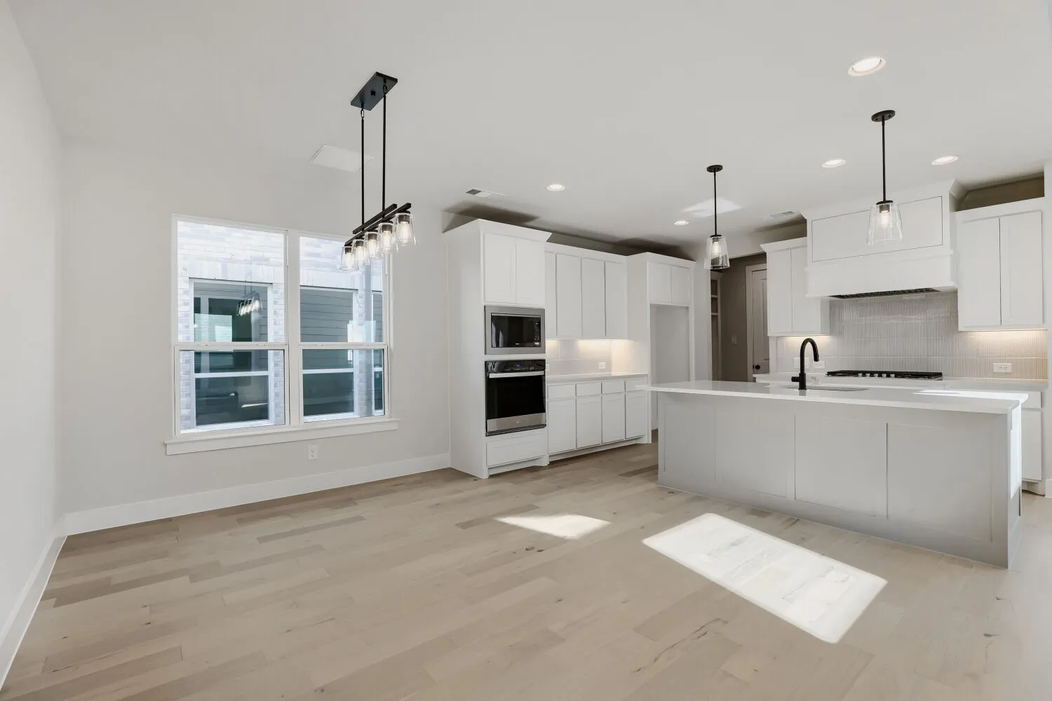 Spacious kitchen and dining area featuring light wood-finish flooring, white cabinetry, a large center island, and contemporary lighting fixtures