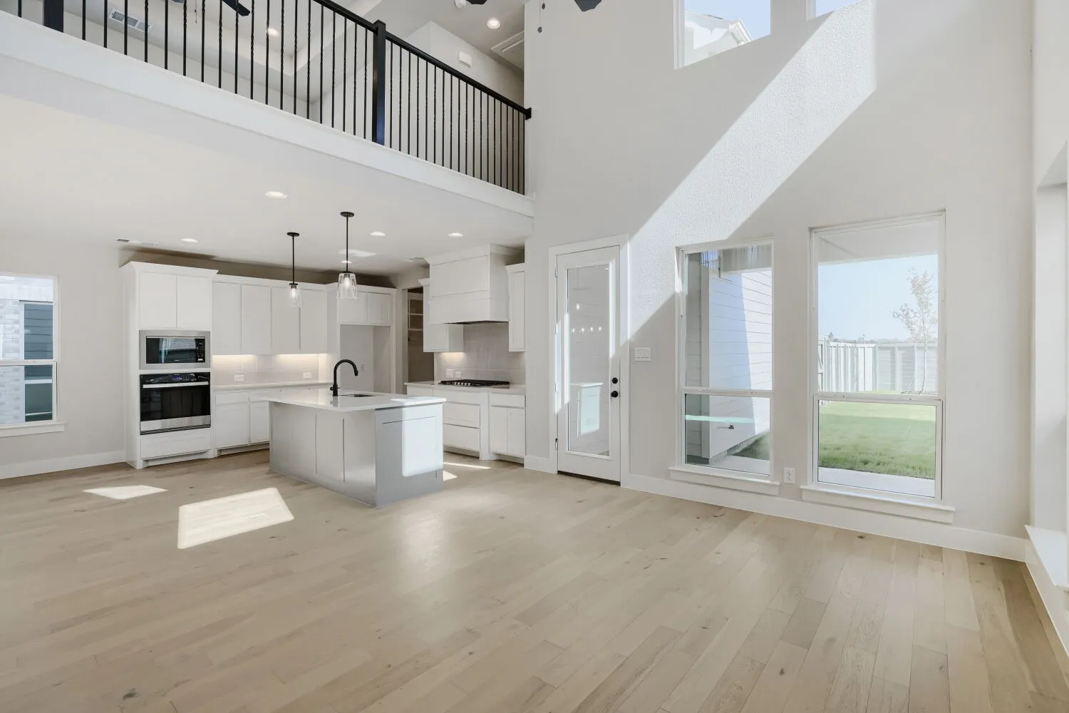 Two-story living area with high ceilings, light wood-finish flooring, and multiple large windows