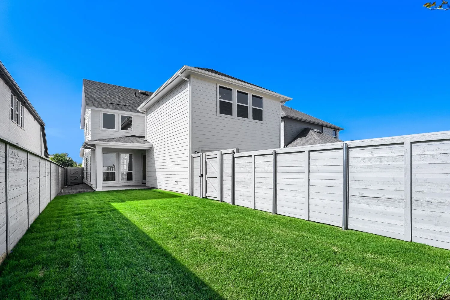 Manicured lawn, full privacy fencing, covered patio, white siding exterior, and dark shingle roofing