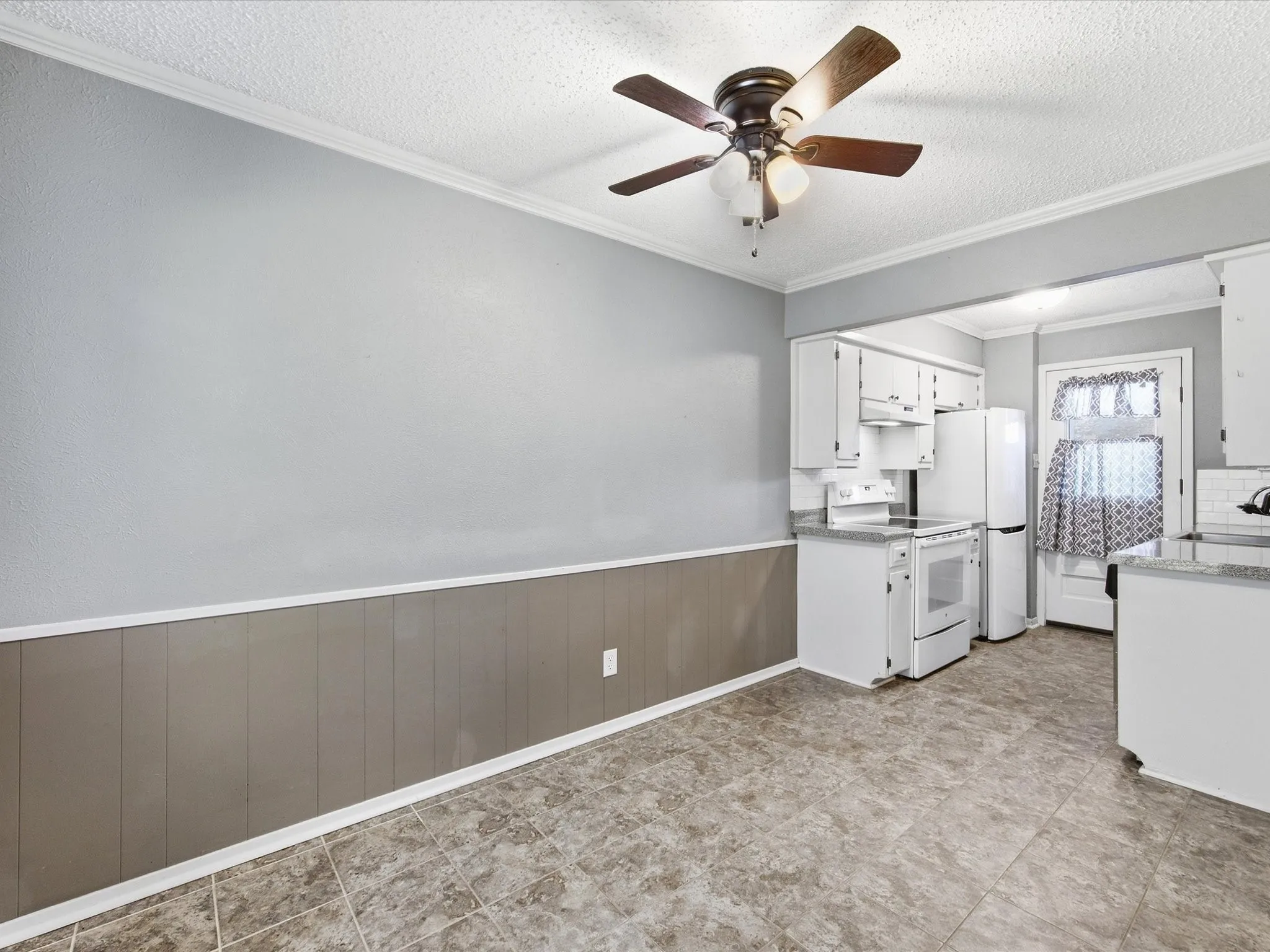 Kitchen with white cabinetry, ceiling fan, tile flooring, and wainscoting