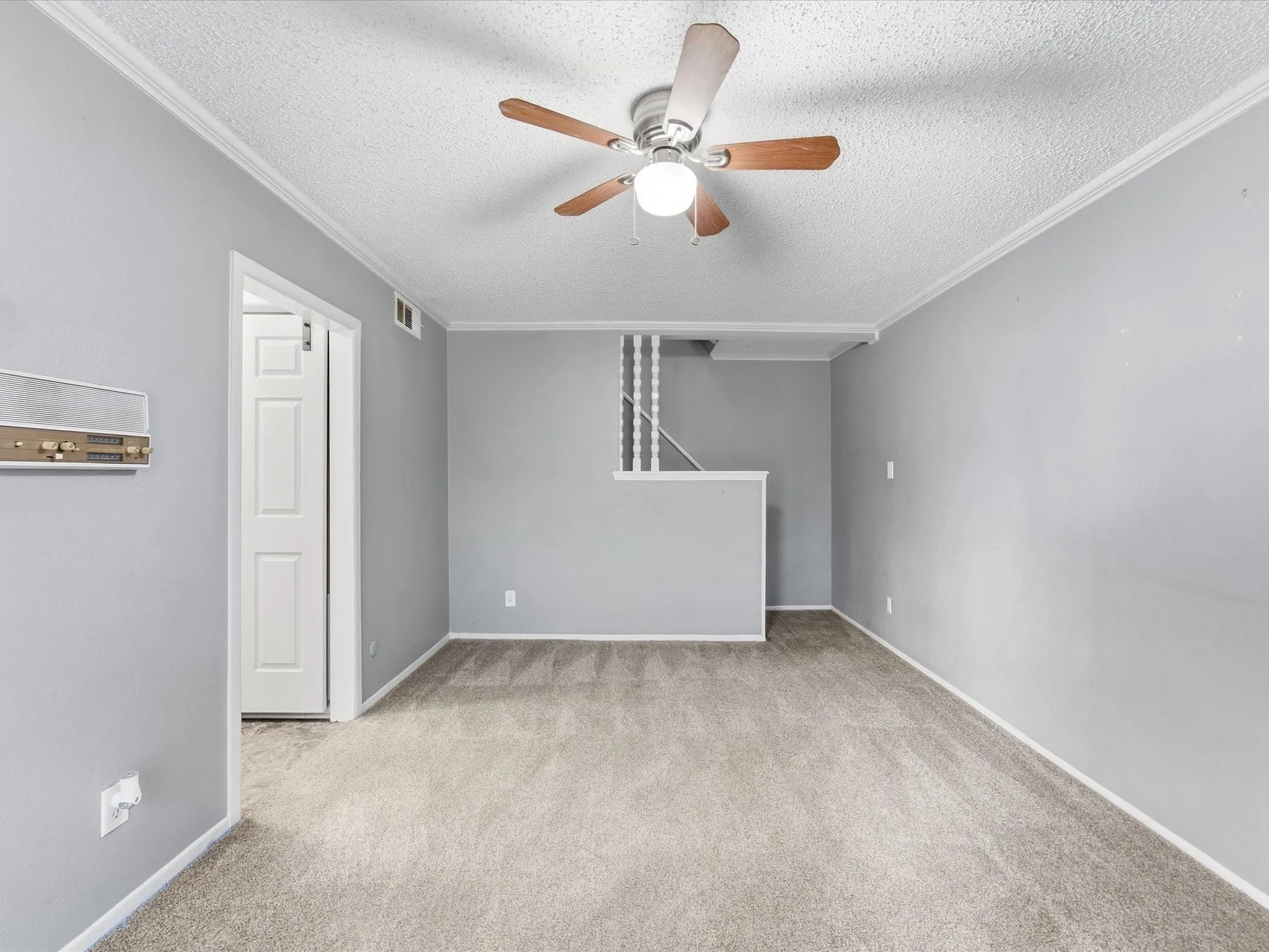 Textured ceiling with crown molding, ceiling fan with light fixture, light gray walls, and light gray carpet