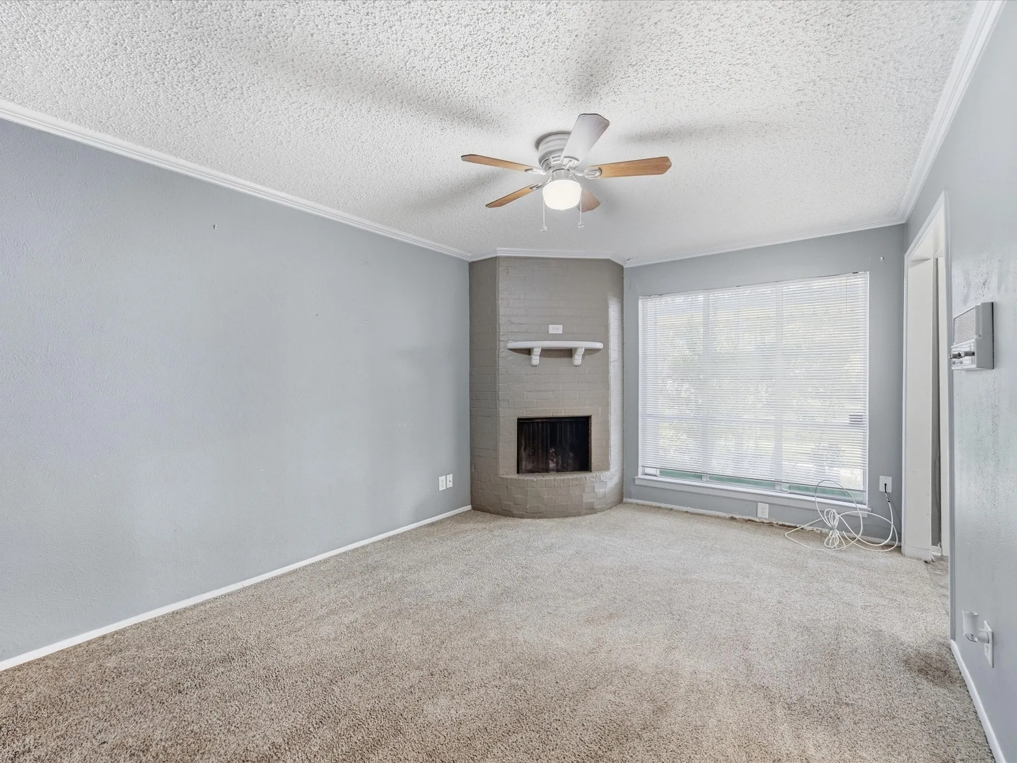 Corner brick fireplace with white mantel, broad window, and ceiling fan