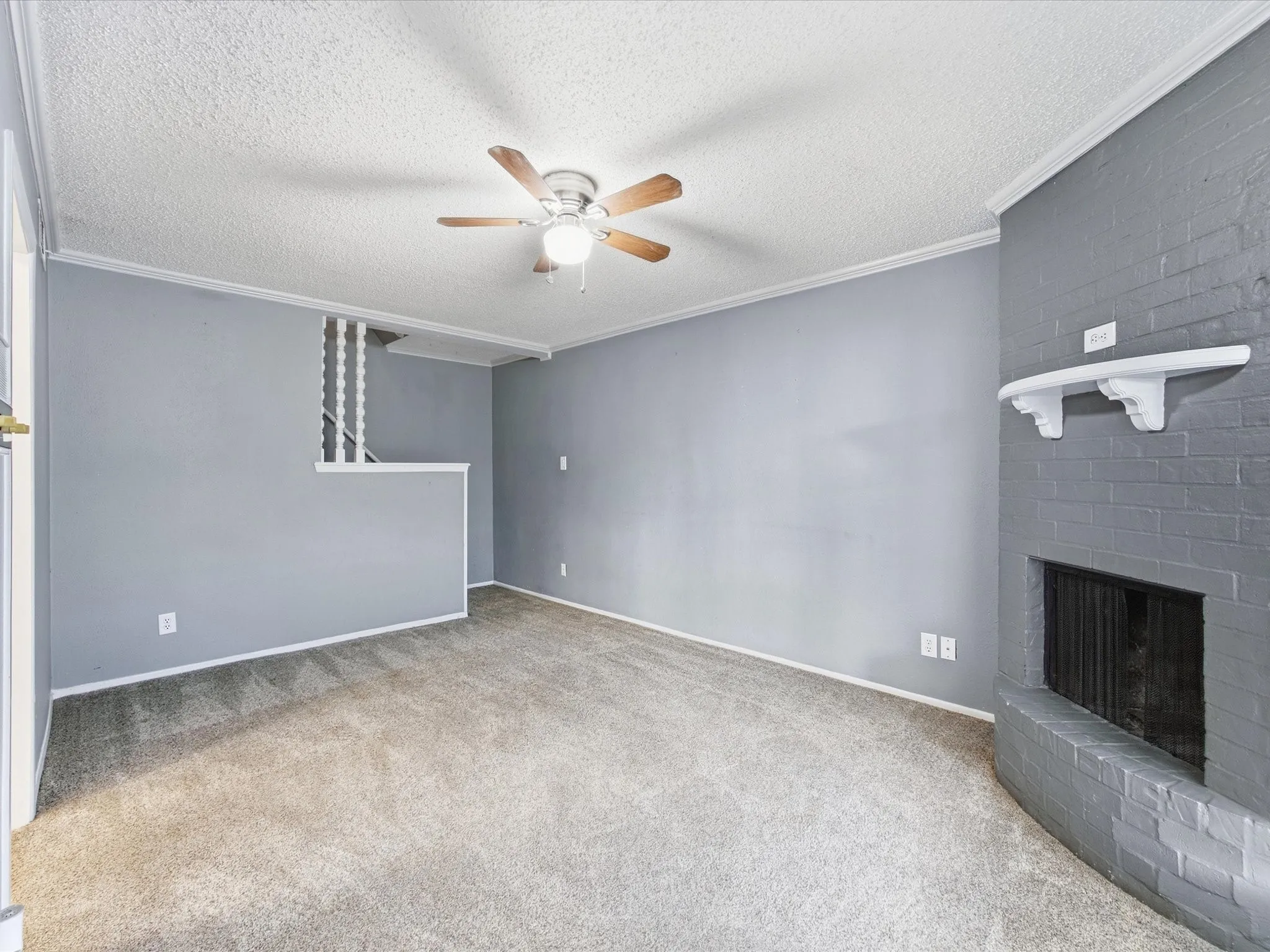 Carpeted living space featuring a ceiling fan with integrated lighting, a painted brick fireplace, and crown molding