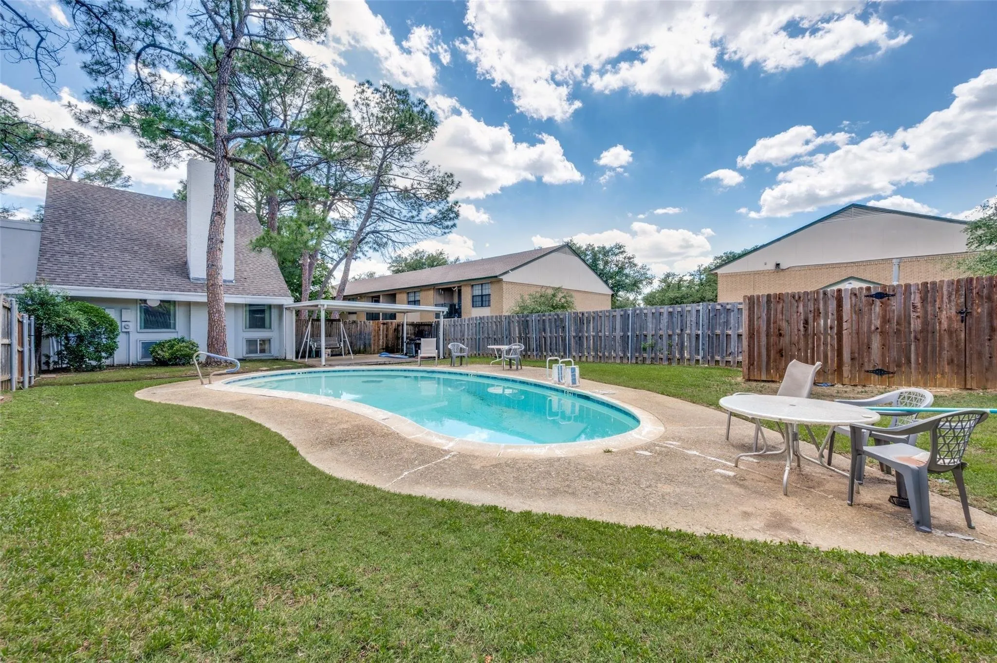Fenced backyard featuring a free-form swimming pool, concrete patio, and established trees