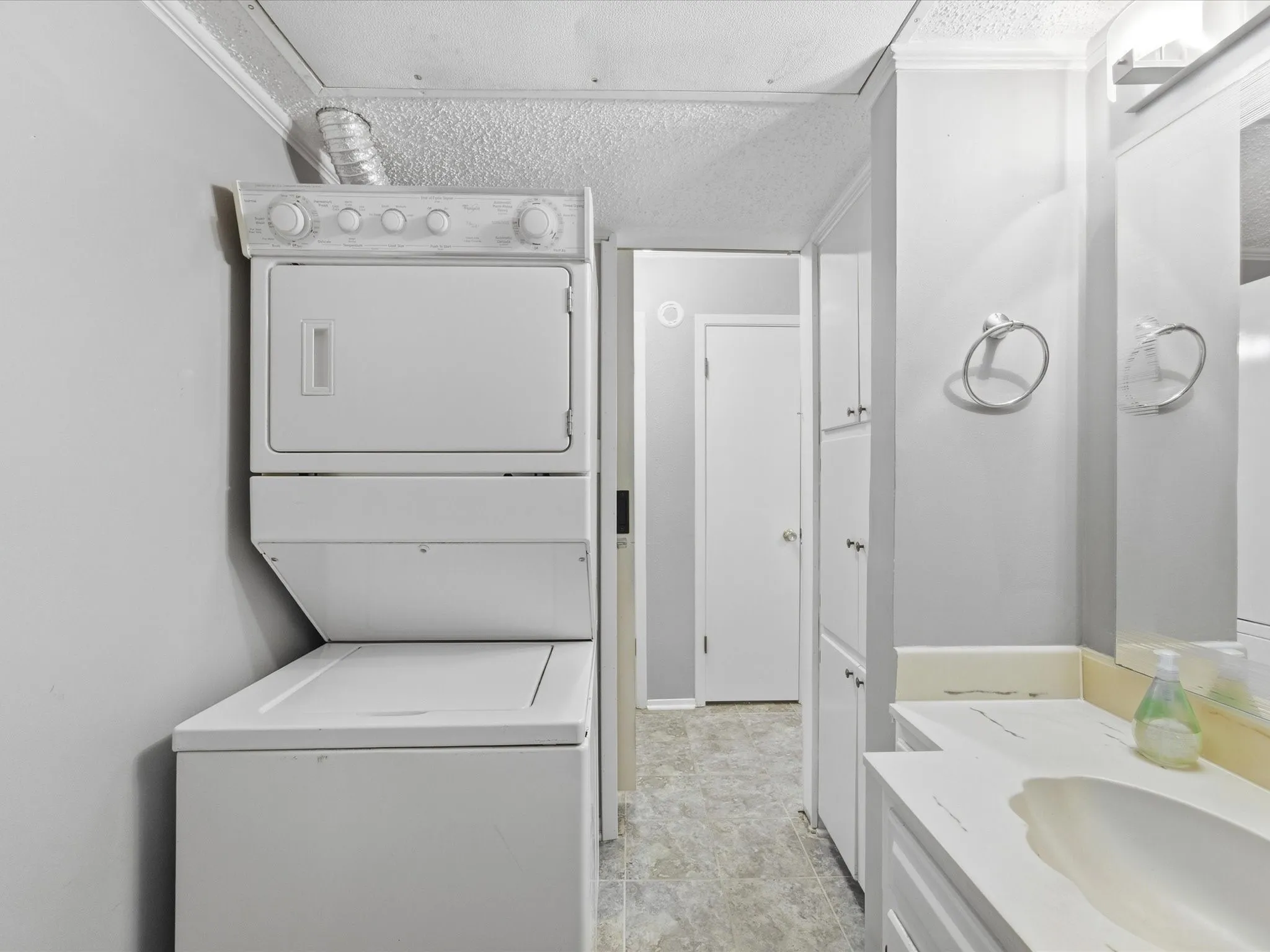 Stackable laundry appliances, built-in cabinetry, vanity with integrated sink, wall-mounted mirror, and vinyl flooring