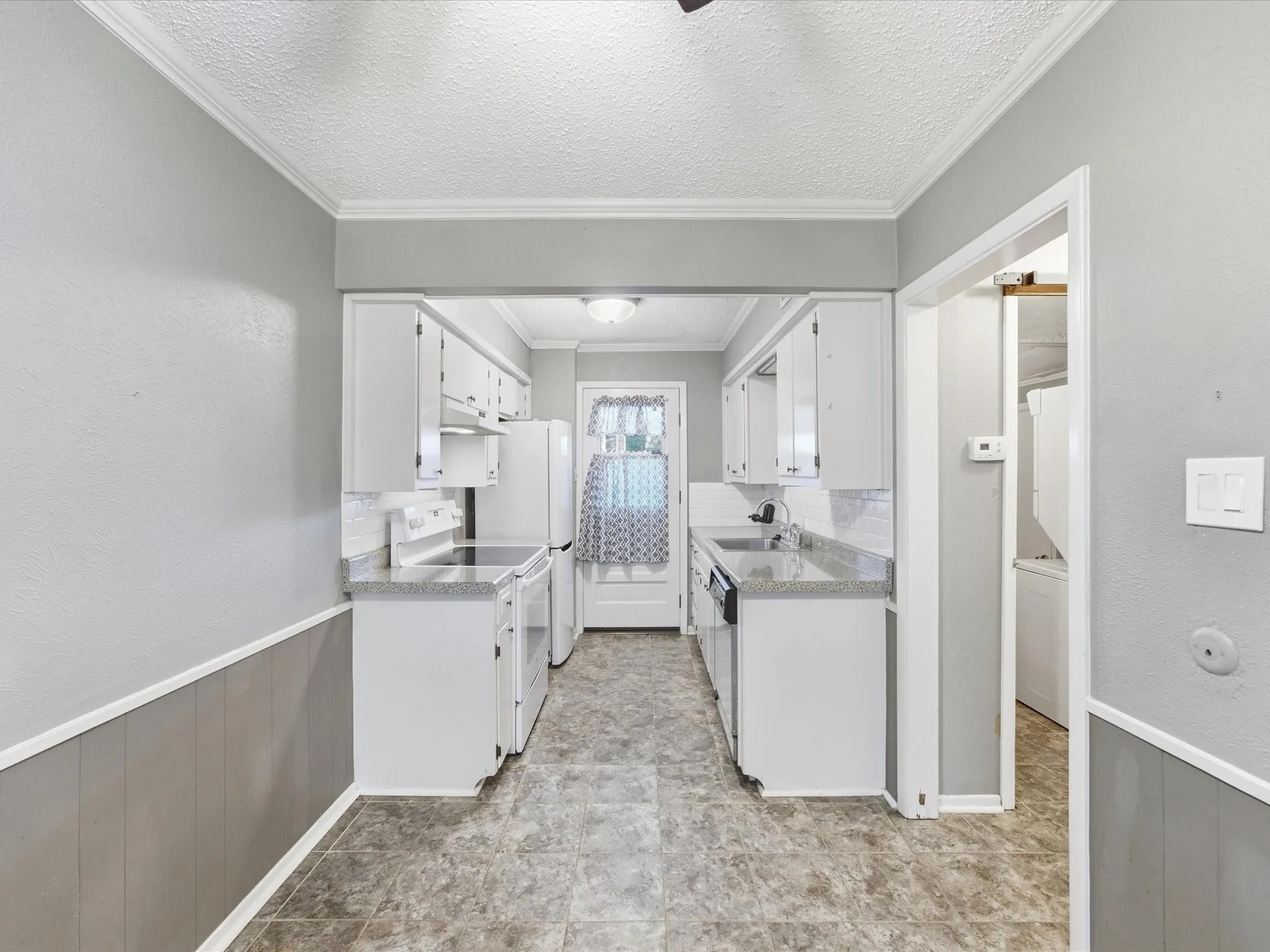 Galley kitchen featuring white cabinetry, gray countertops, and white appliances