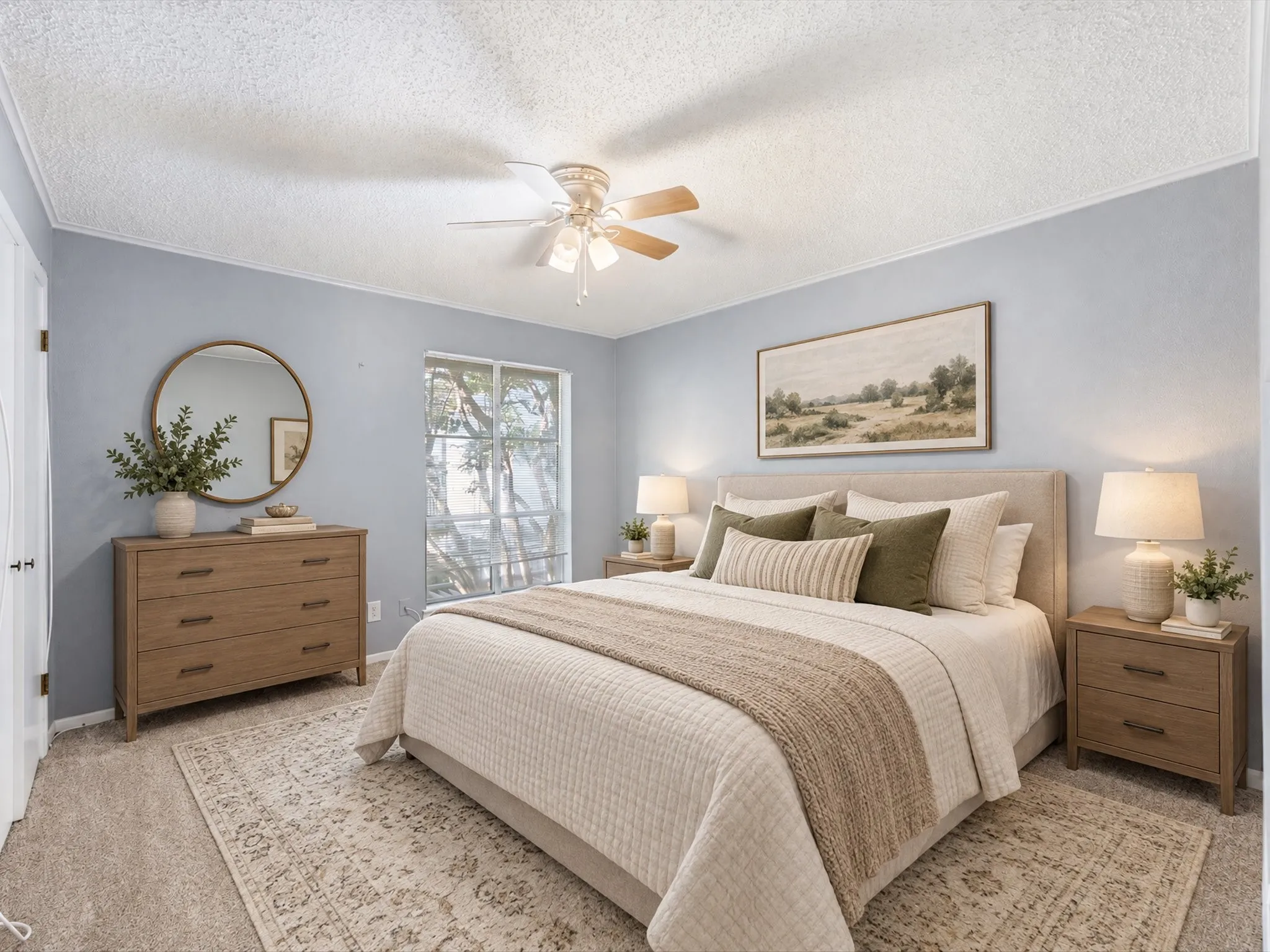 Serene primary bedroom showcasing soft periwinkle walls, a upholstered bed frame with neutral bedding, dual nightstands with integrated lighting, hardwood-finish dresser with round mirror accent, ceiling fan with light fixture, and access to a sliding glass door leading to outdoor space