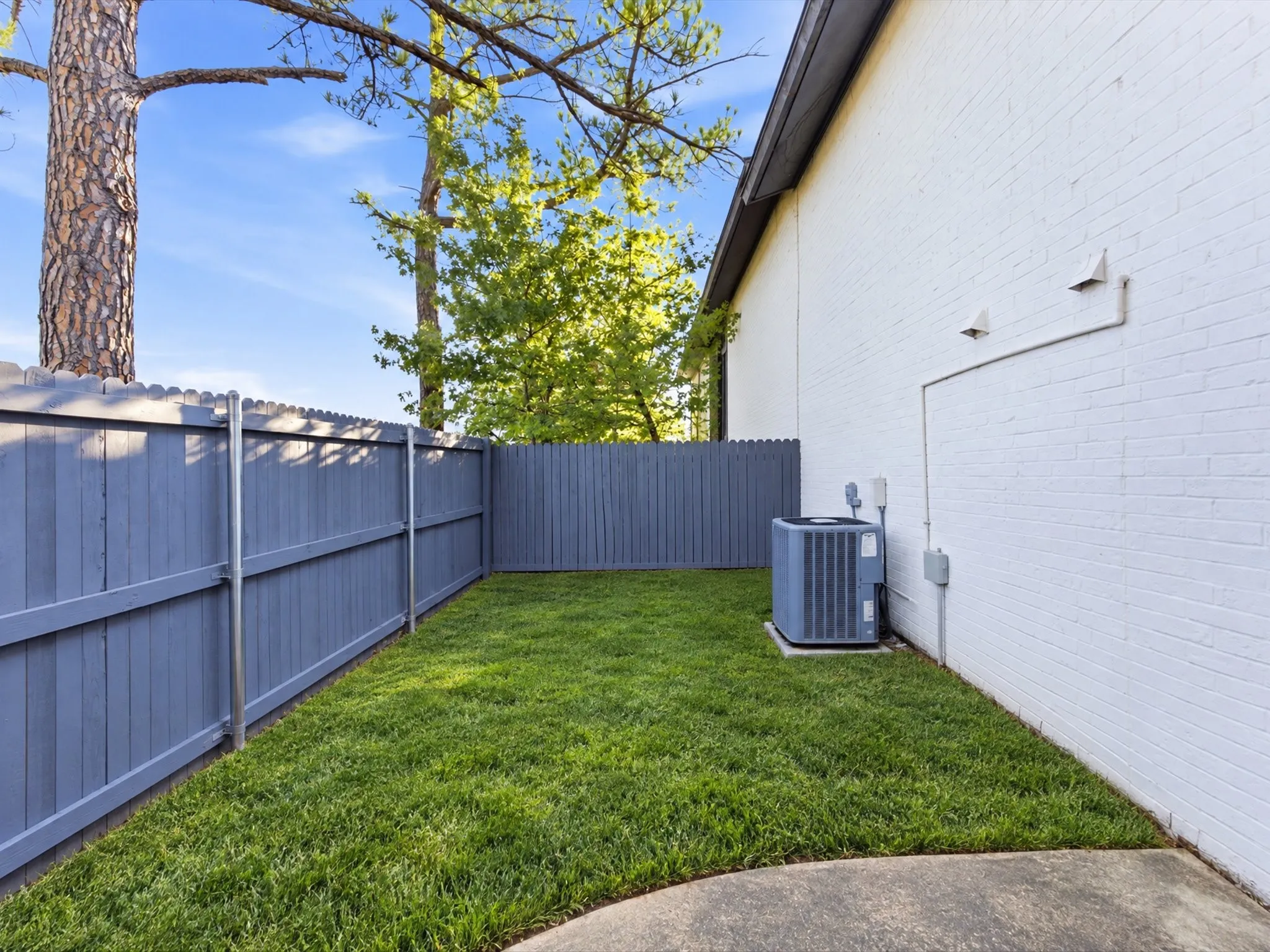 Private yard featuring a painted wood fence, manicured lawn, and concrete patio