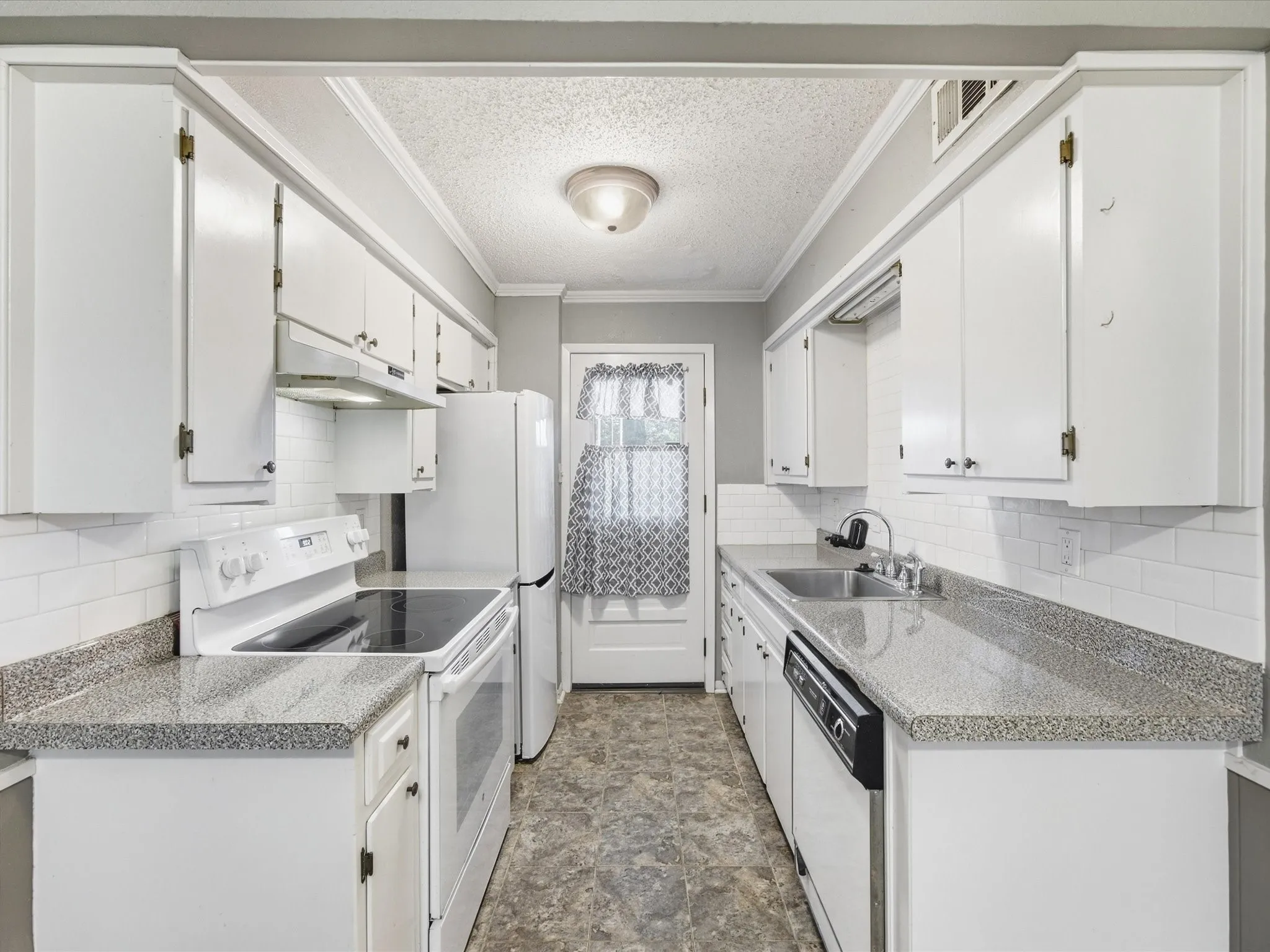 White cabinetry and appliances, grey speckled countertops, white subway tile backsplash, and a stainless steel sink