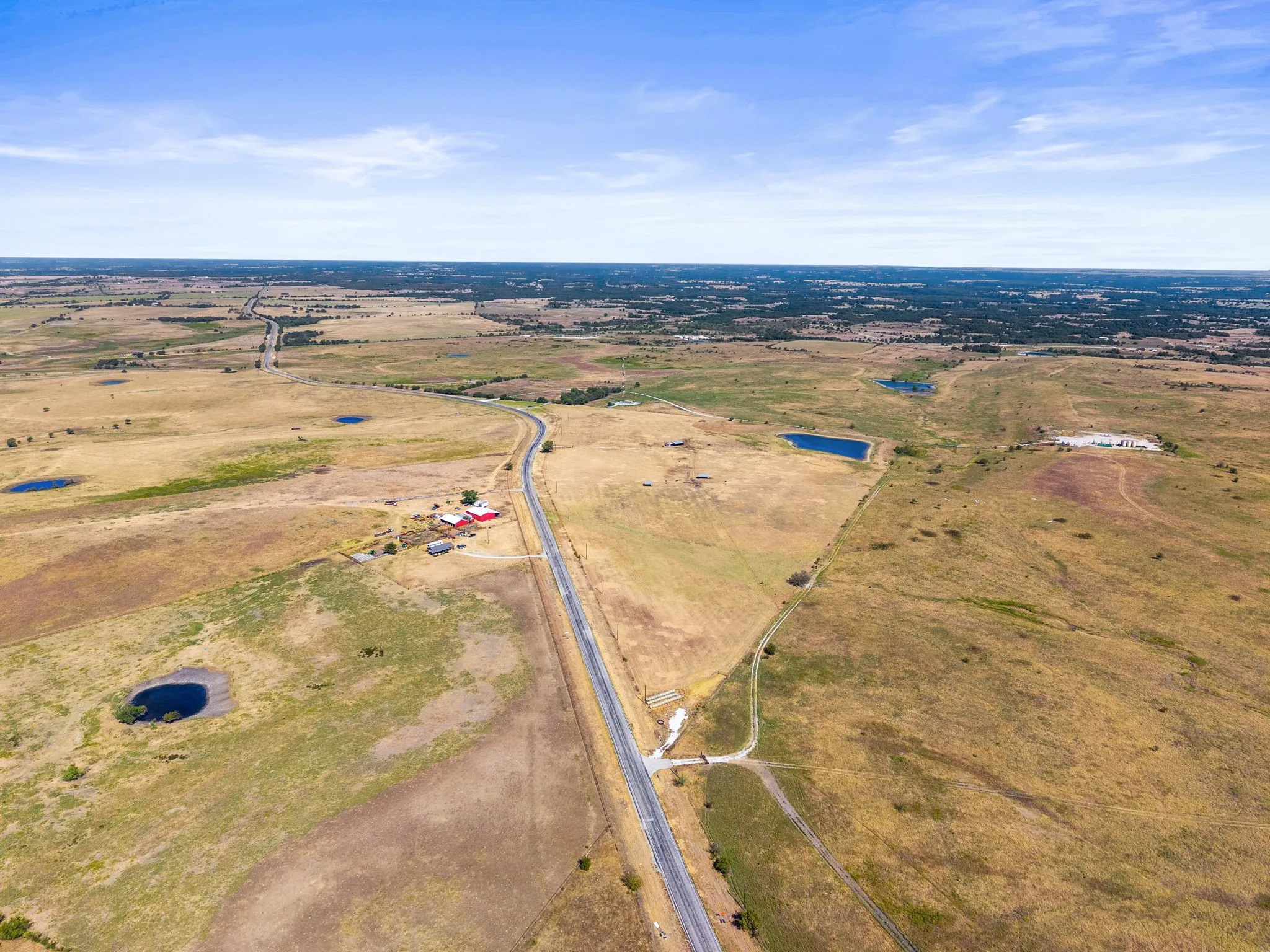 Expansive land with a paved road, multiple ponds, and distant structures