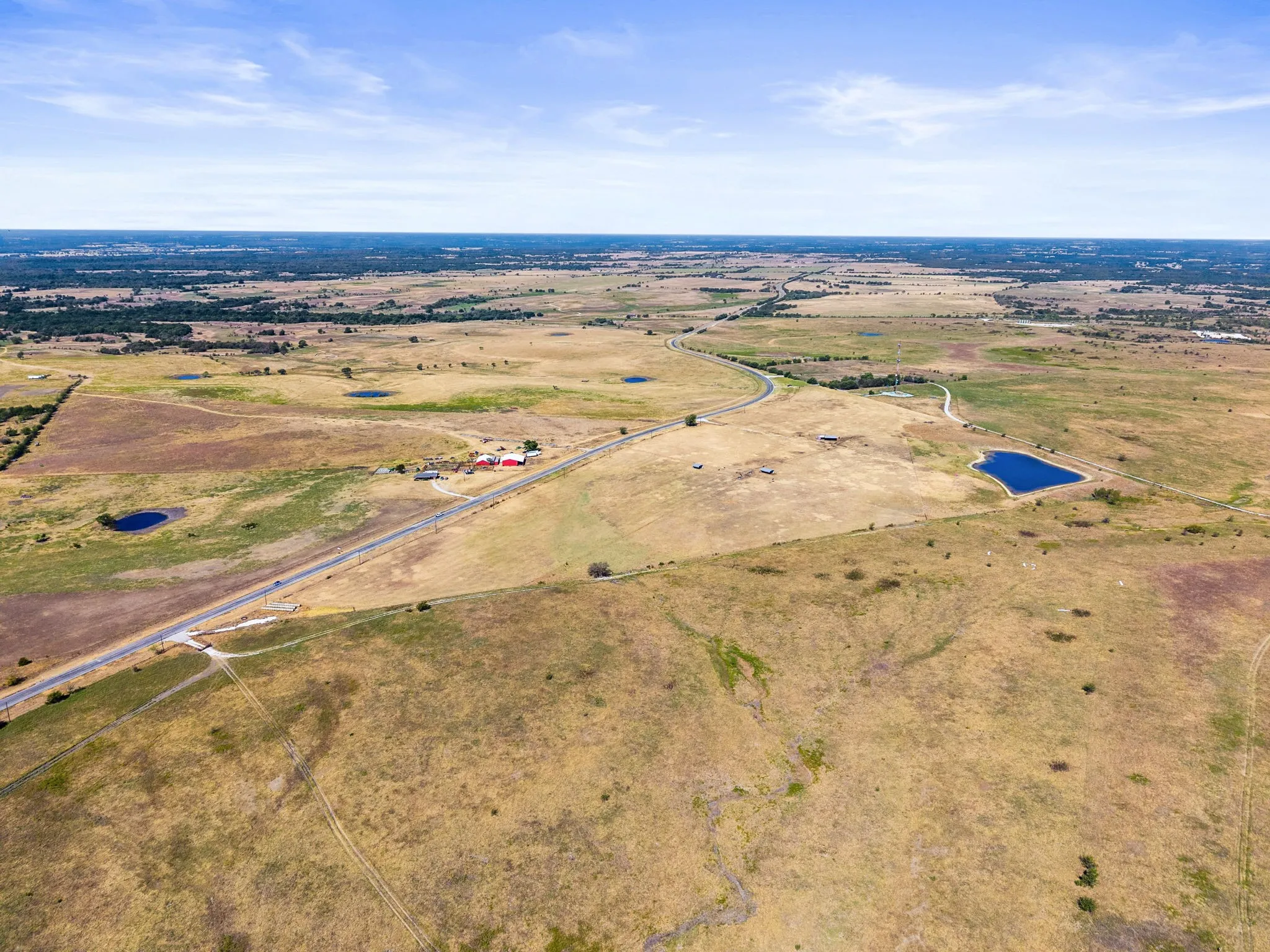 Expansive open terrain with multiple ponds, a paved road, and distant structures
