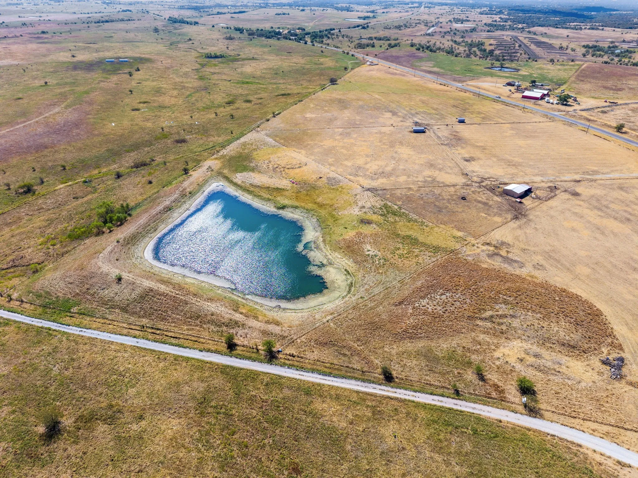 Expansive agricultural land featuring a prominent pond and a defined road