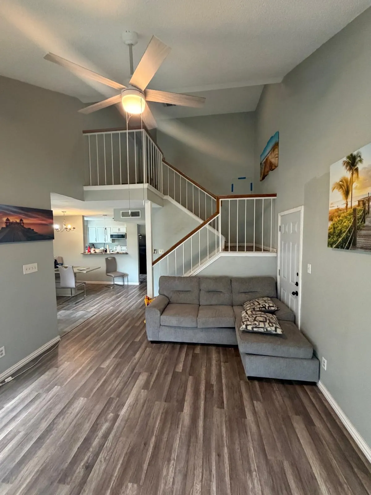 Vaulted ceiling with a contemporary ceiling fan, wood-finish flooring, and a multi-level staircase with white railing