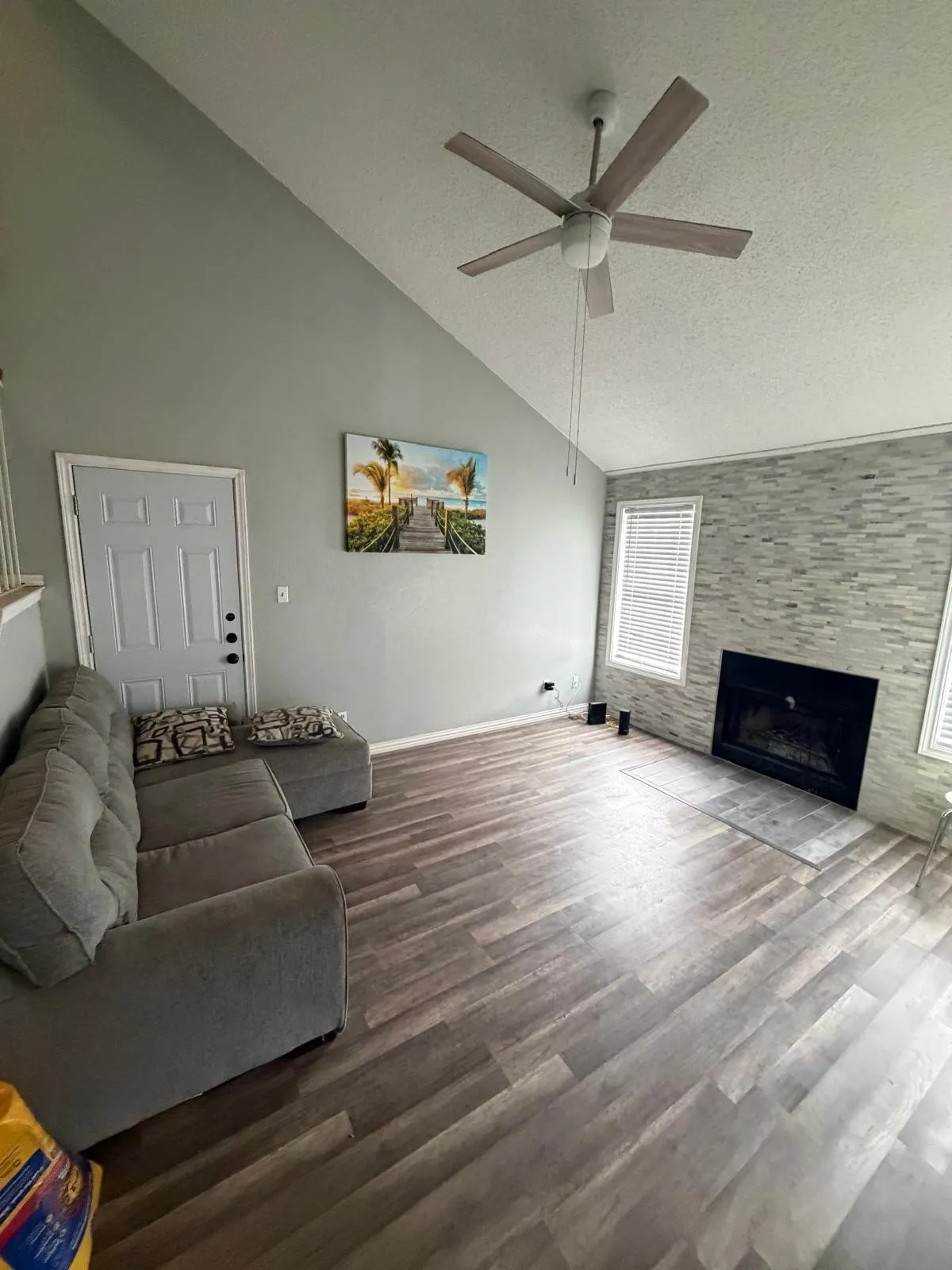 Vaulted ceiling, wood-finish flooring, ceiling fan, fireplace with tile surround, and white paneled door