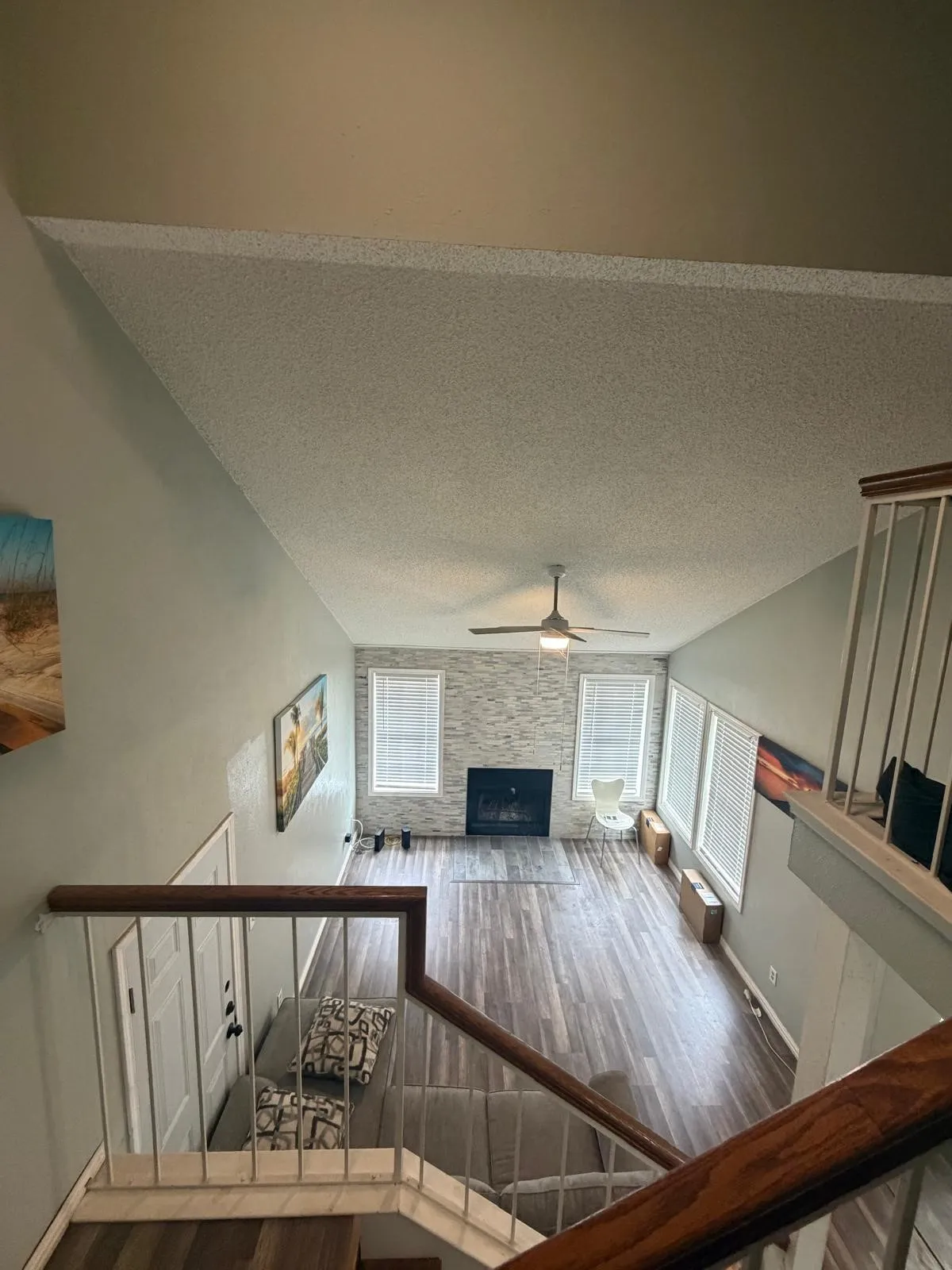 Vaulted ceiling with a ceiling fan, fireplace with a stacked stone surround, wood-finish flooring, and white window blinds