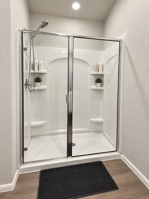 Enclosed shower featuring a handheld showerhead, built-in shelving, and a clear glass sliding door