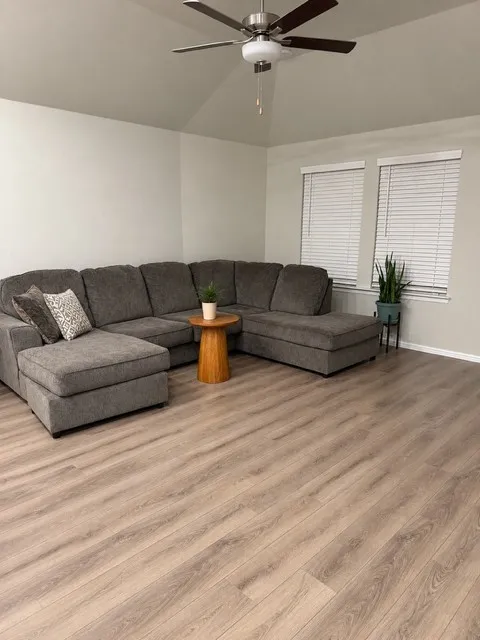 Vaulted ceiling, wood-finish flooring, ceiling fan with integrated lighting, and two windows with blinds