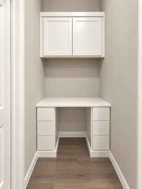 Built-in desk with a white countertop, coordinating cabinetry, and wood-finish flooring