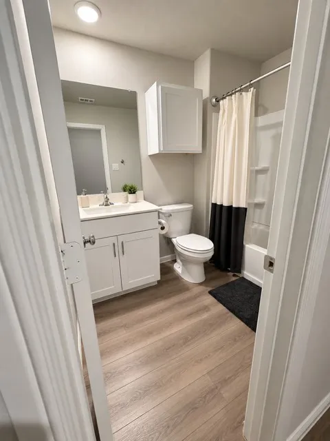Bathroom featuring wood-finish flooring, a white vanity with double-door cabinetry, and a full bathtub with shower